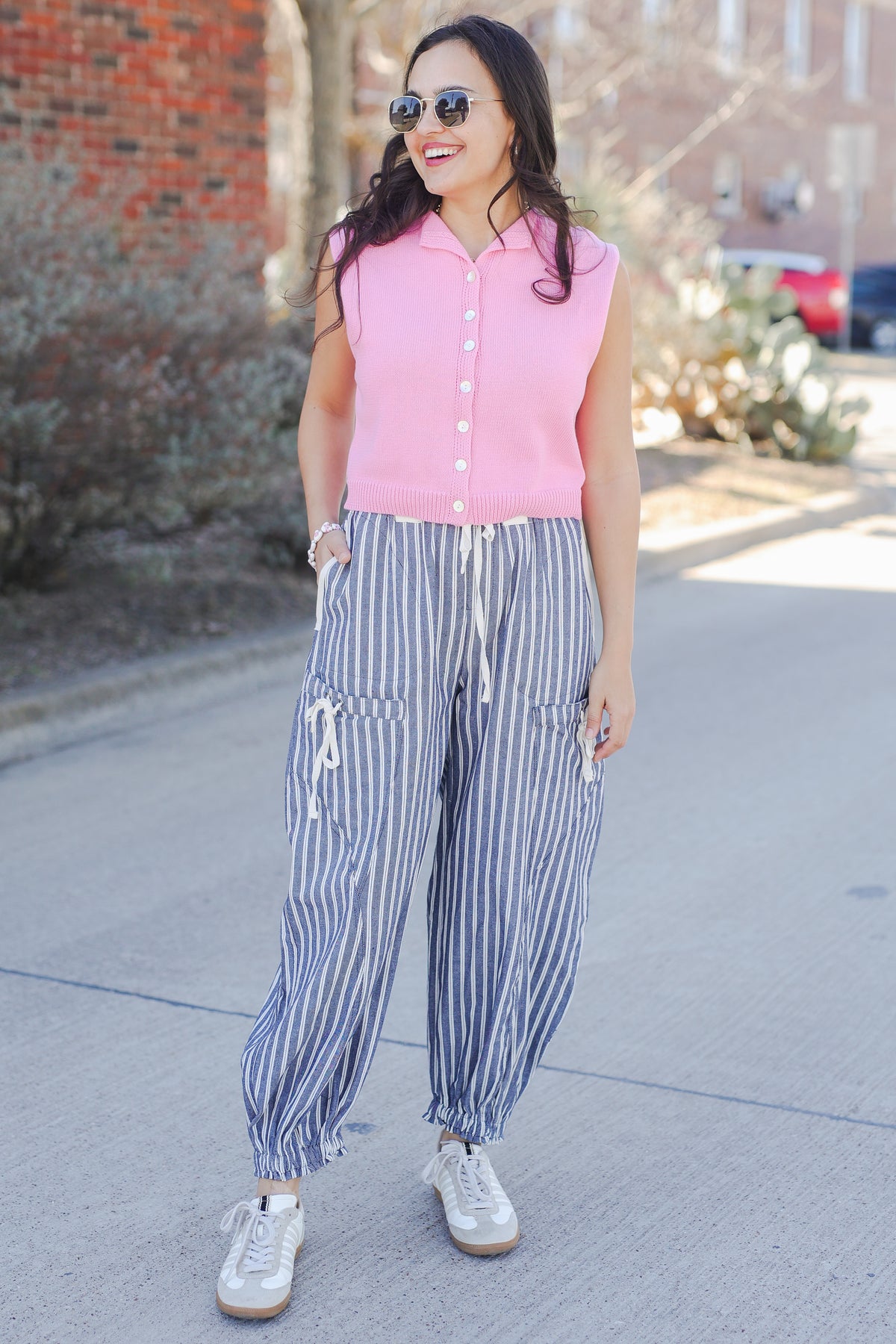 Woman wearing a pink sweater tank and blue and white striped pants outside.