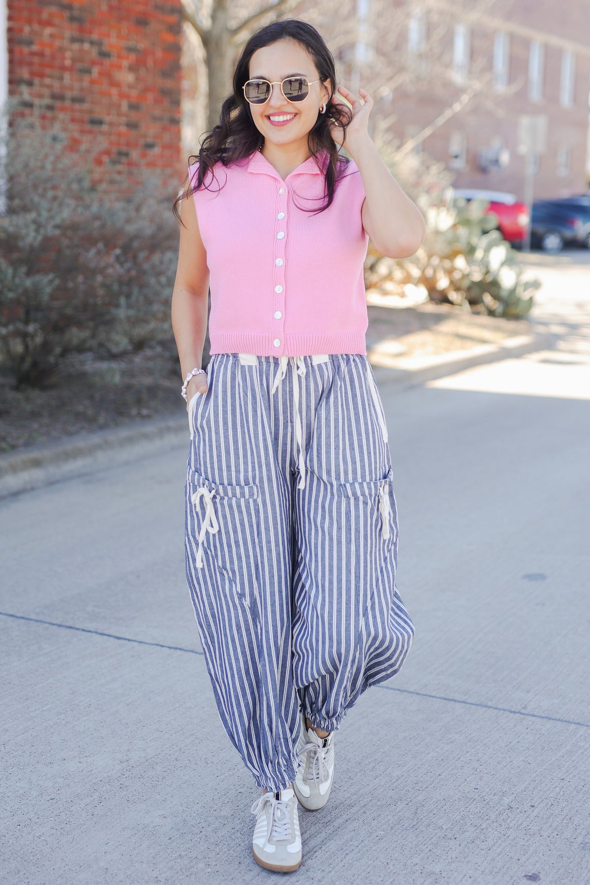 Woman wearing a pink sweater tank and blue and whit striped pants outside.