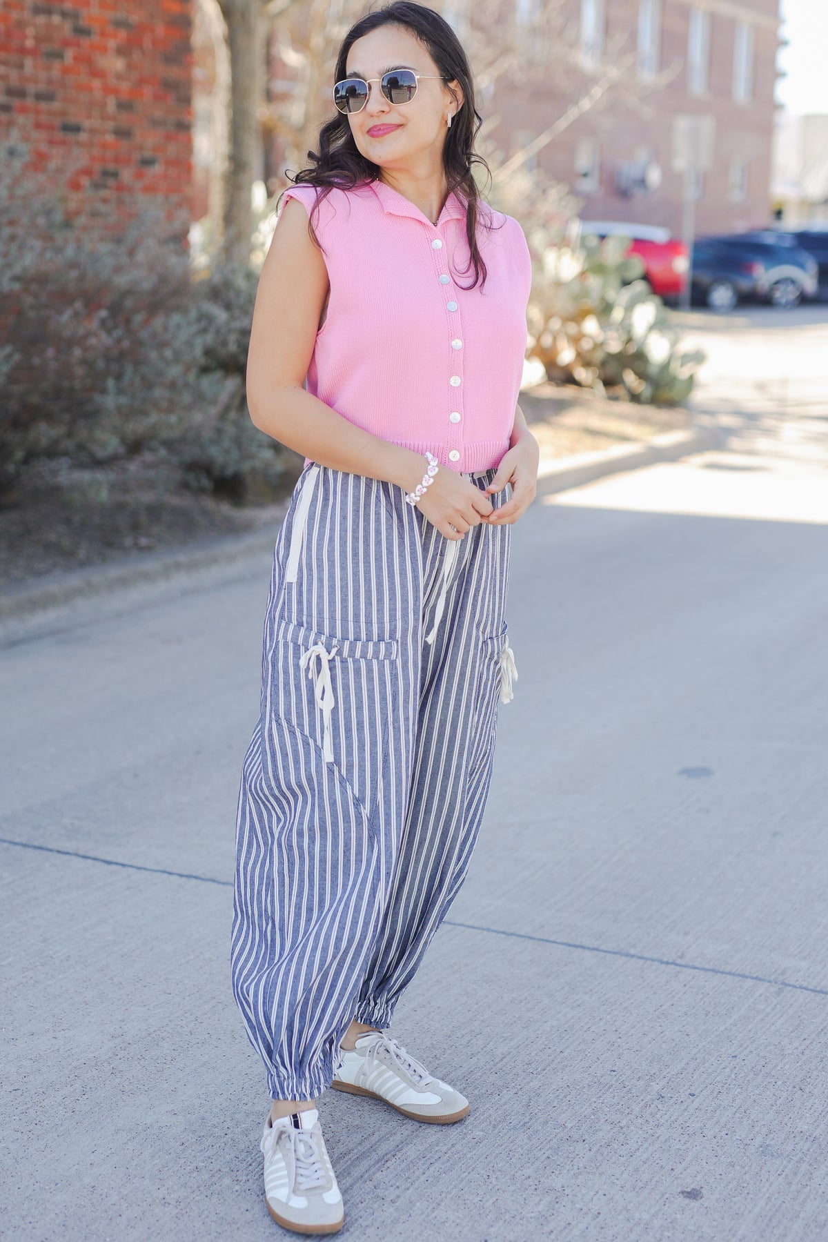 Woman wearing a pink sweater tank and blue and white striped pants outside.