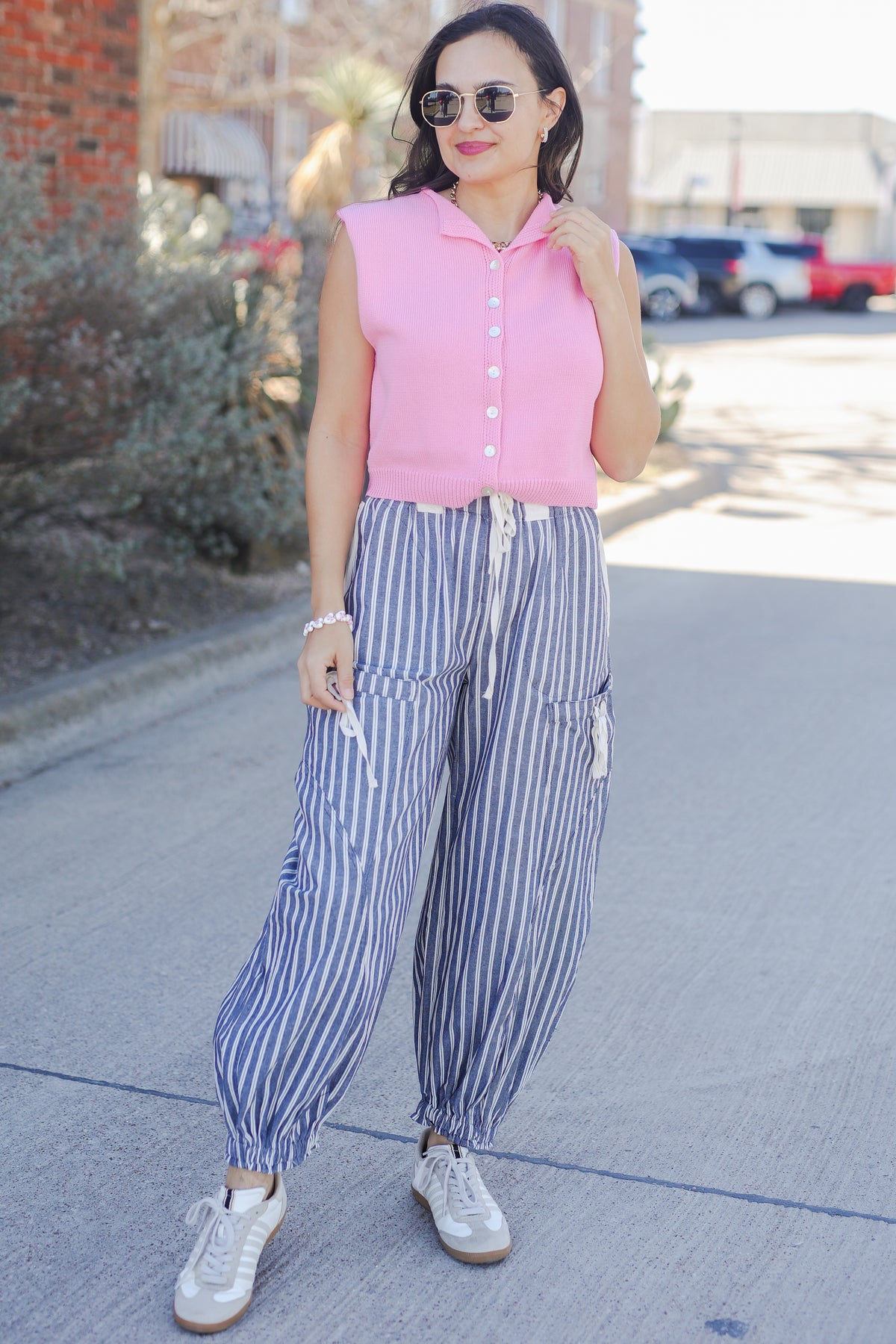 Woman wearing a pink sleeveless top and striped pants on a sidewalk.