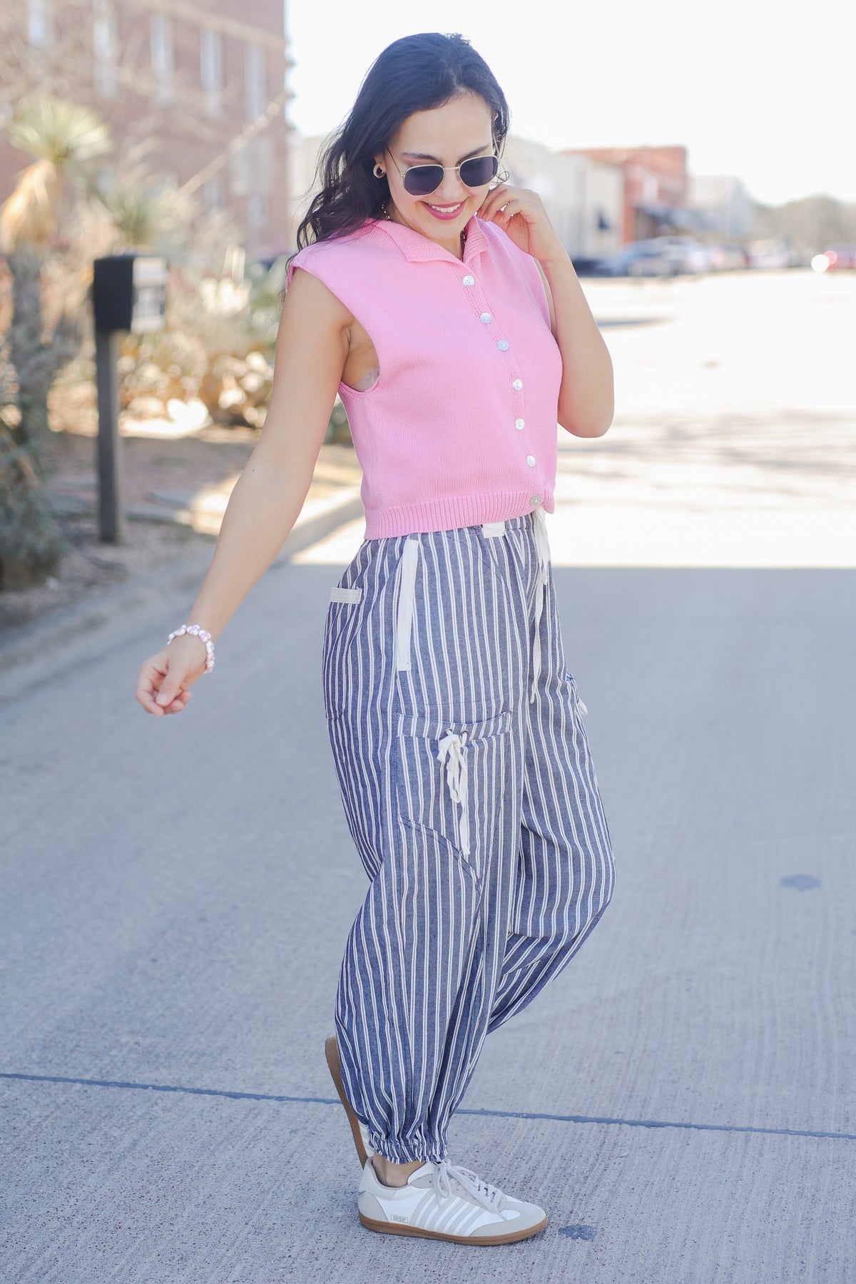 Woman wearing a pink sleeveless top and striped pants on a street.