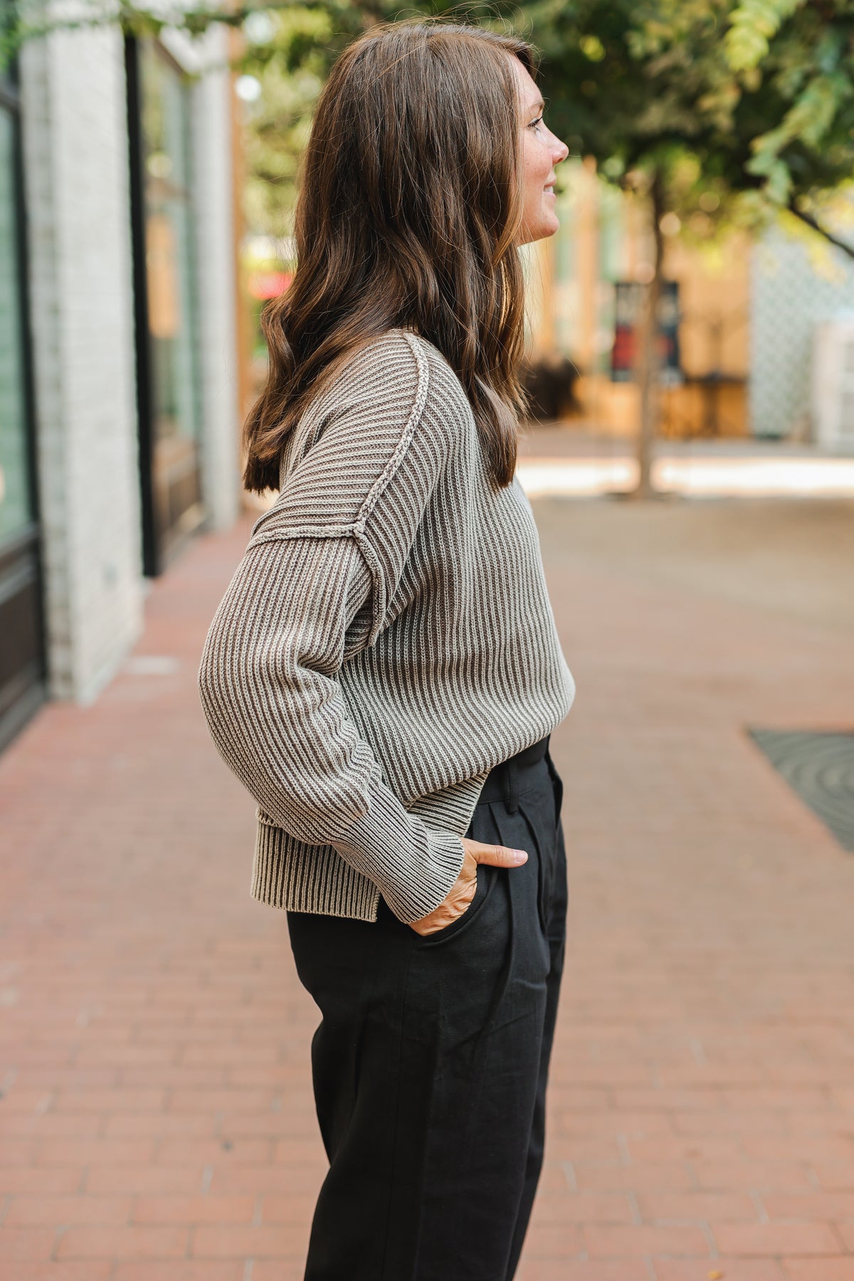 Woman wearing a beige sweater and black pants walking on a sidewalk.