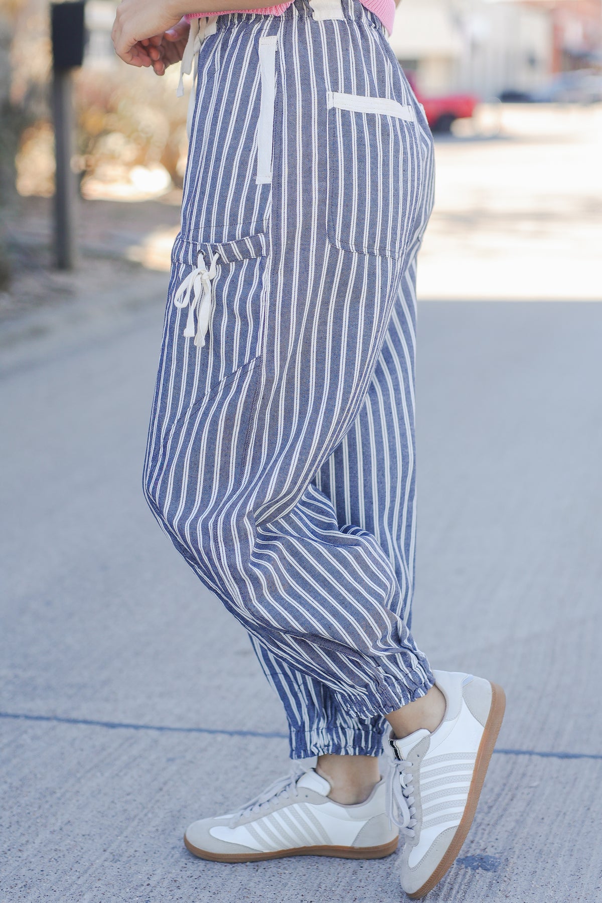 Person wearing blue and white striped pants with white sneakers on a blurred street background