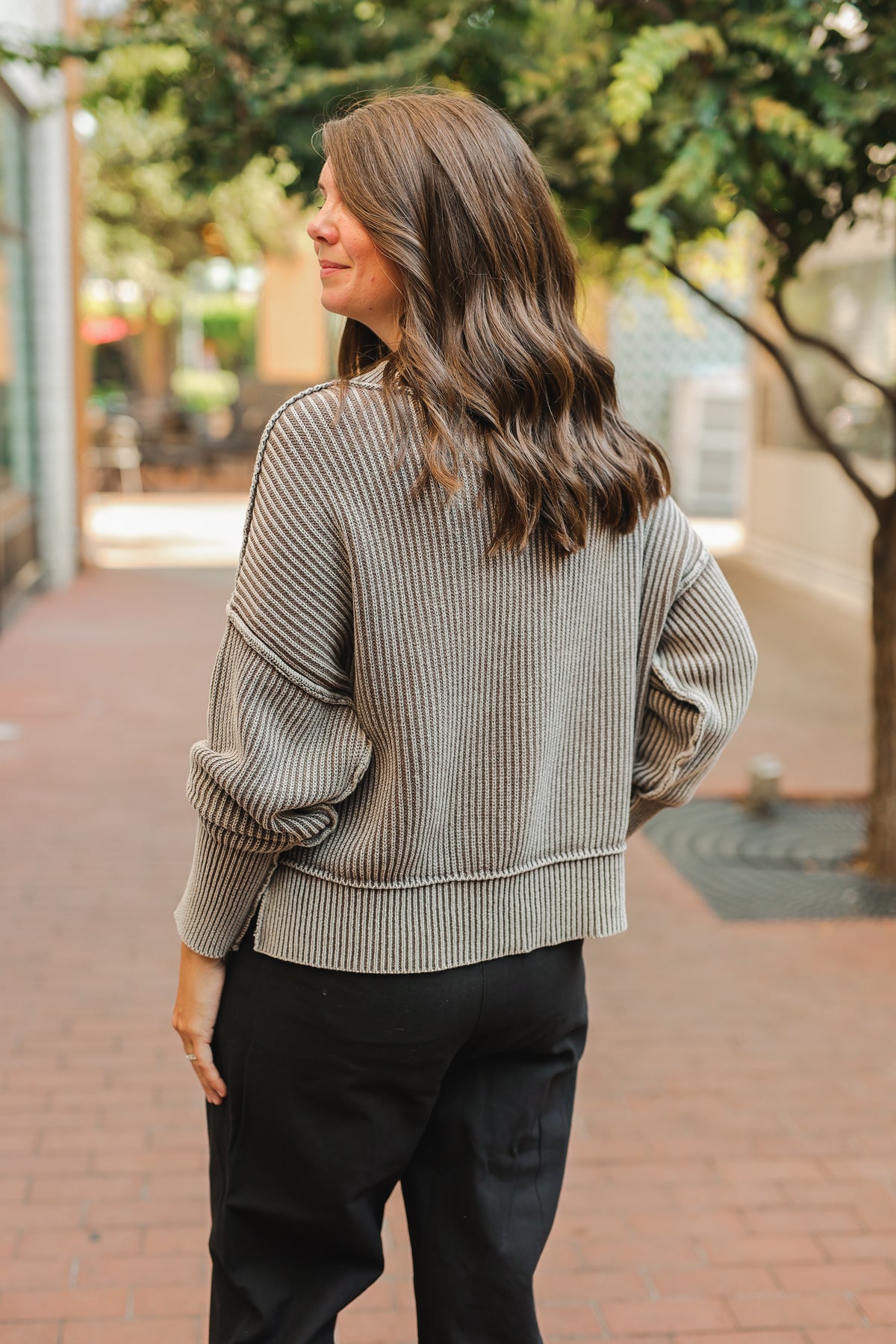 Woman wearing a striped sweater and black pants walking on a sidewalk.