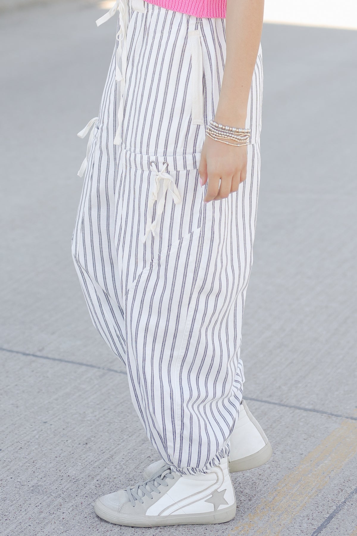 Person wearing white and gray striped pants with white sneakers on a pavement background