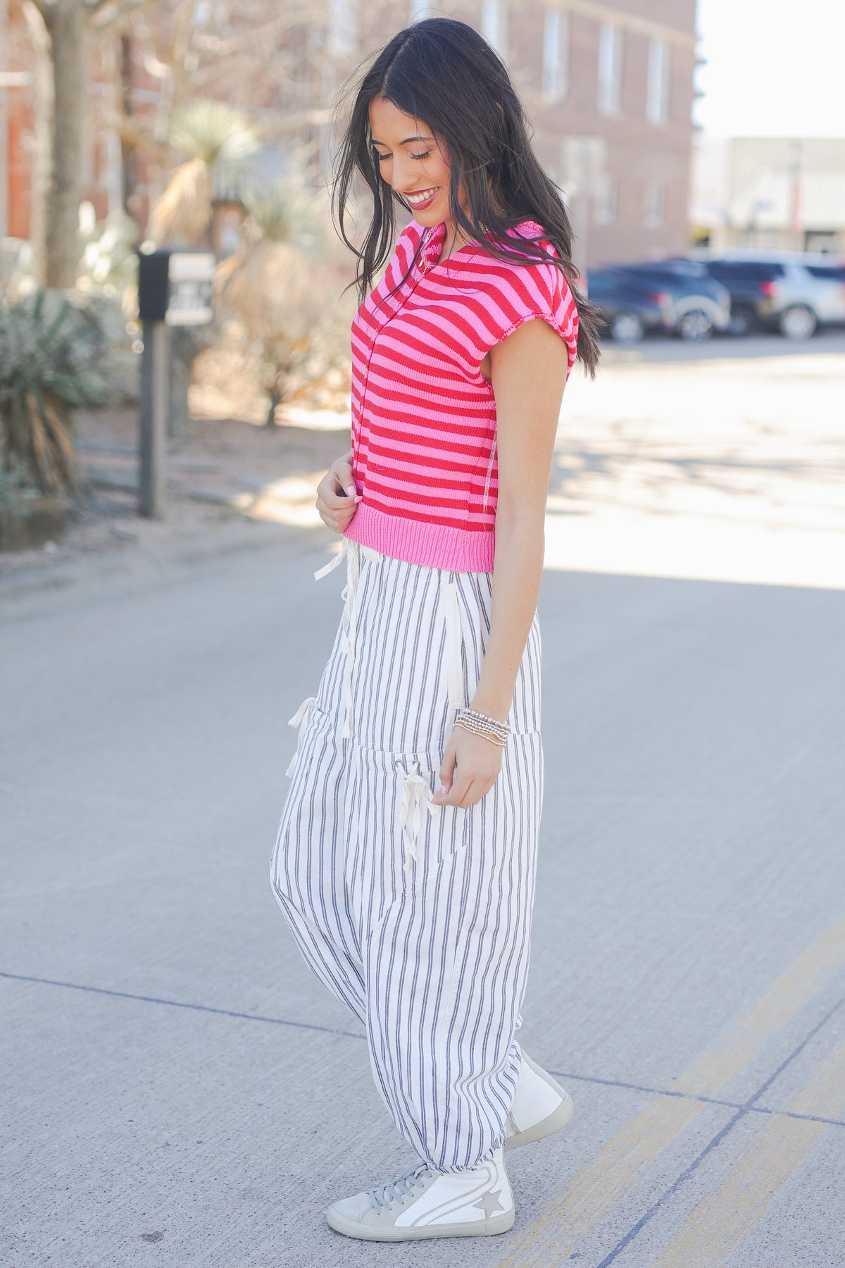 Woman wearing a pink striped shirt and white pants on a city street.