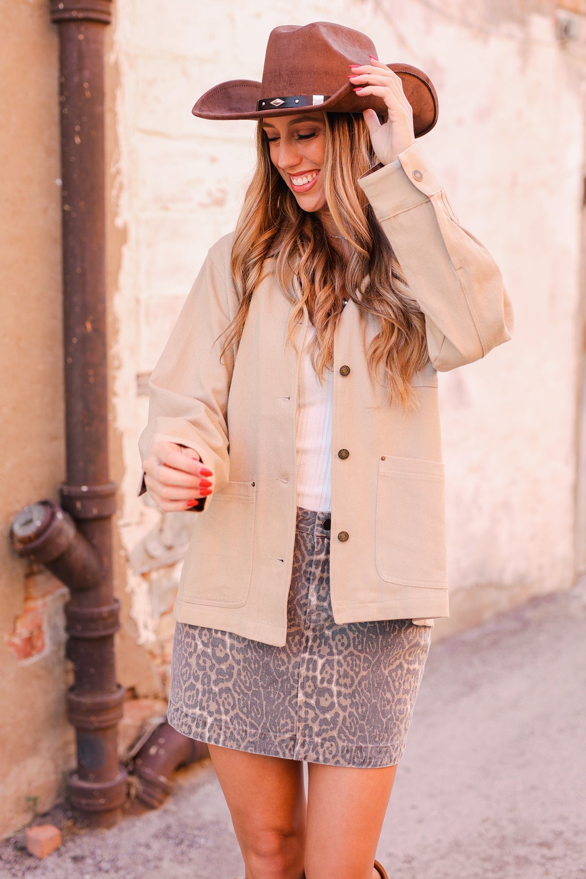 Woman wearing a beige jacket and brown hat against a neutral wall.