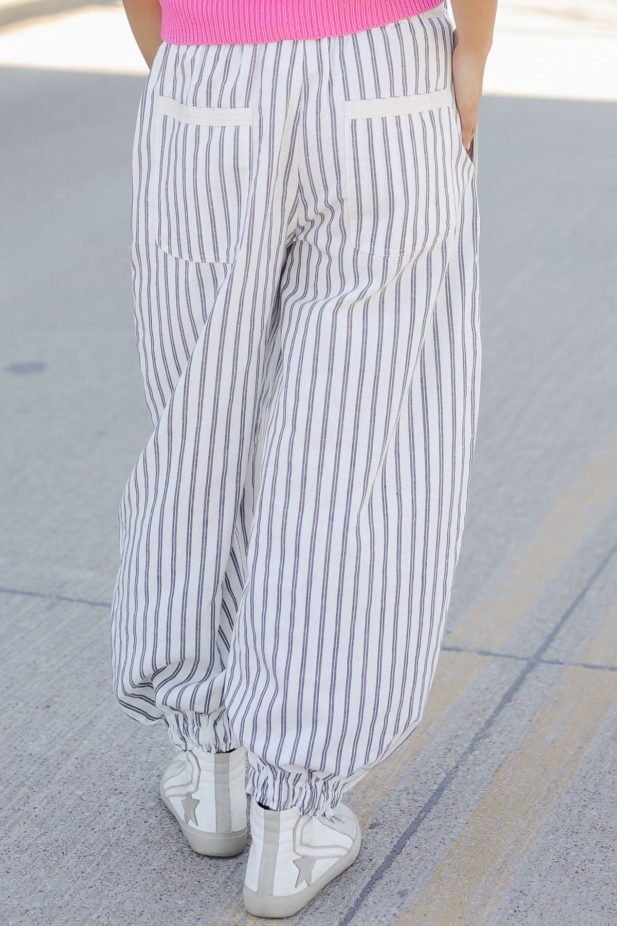Person wearing striped pants and white sneakers on a pavement background