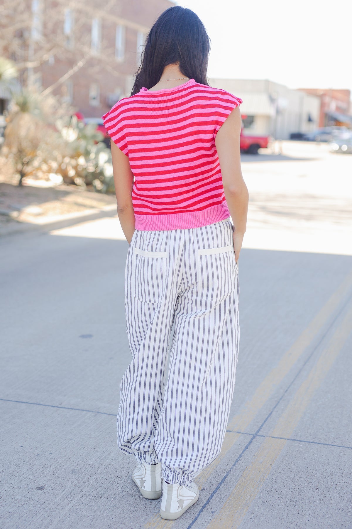 Person wearing a pink striped shirt and white pants on a street.