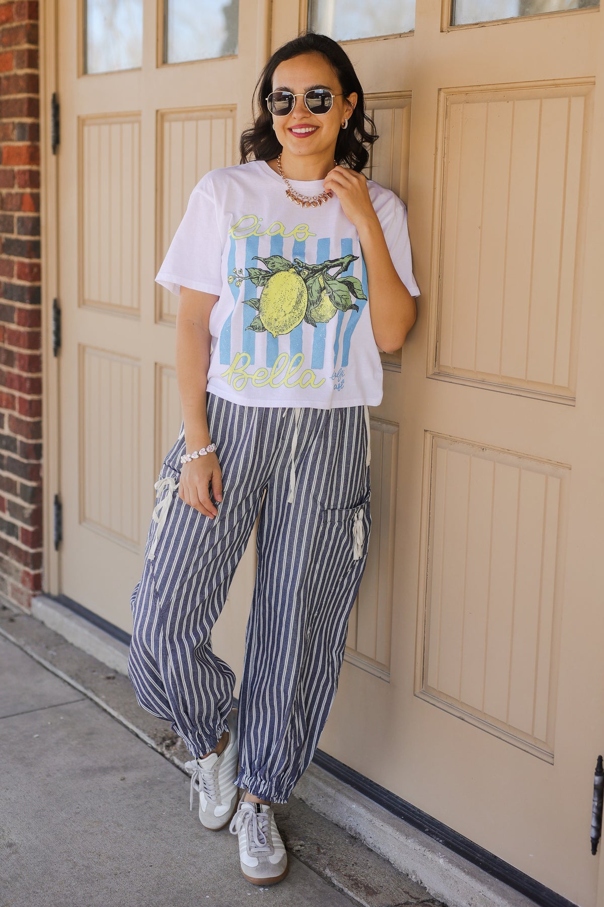 Woman wearing a graphic t-shirt and striped pants standing in front of a door.