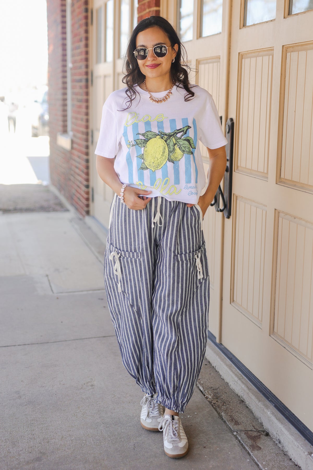 Woman wearing a graphic t-shirt and striped pants standing in front of a door.