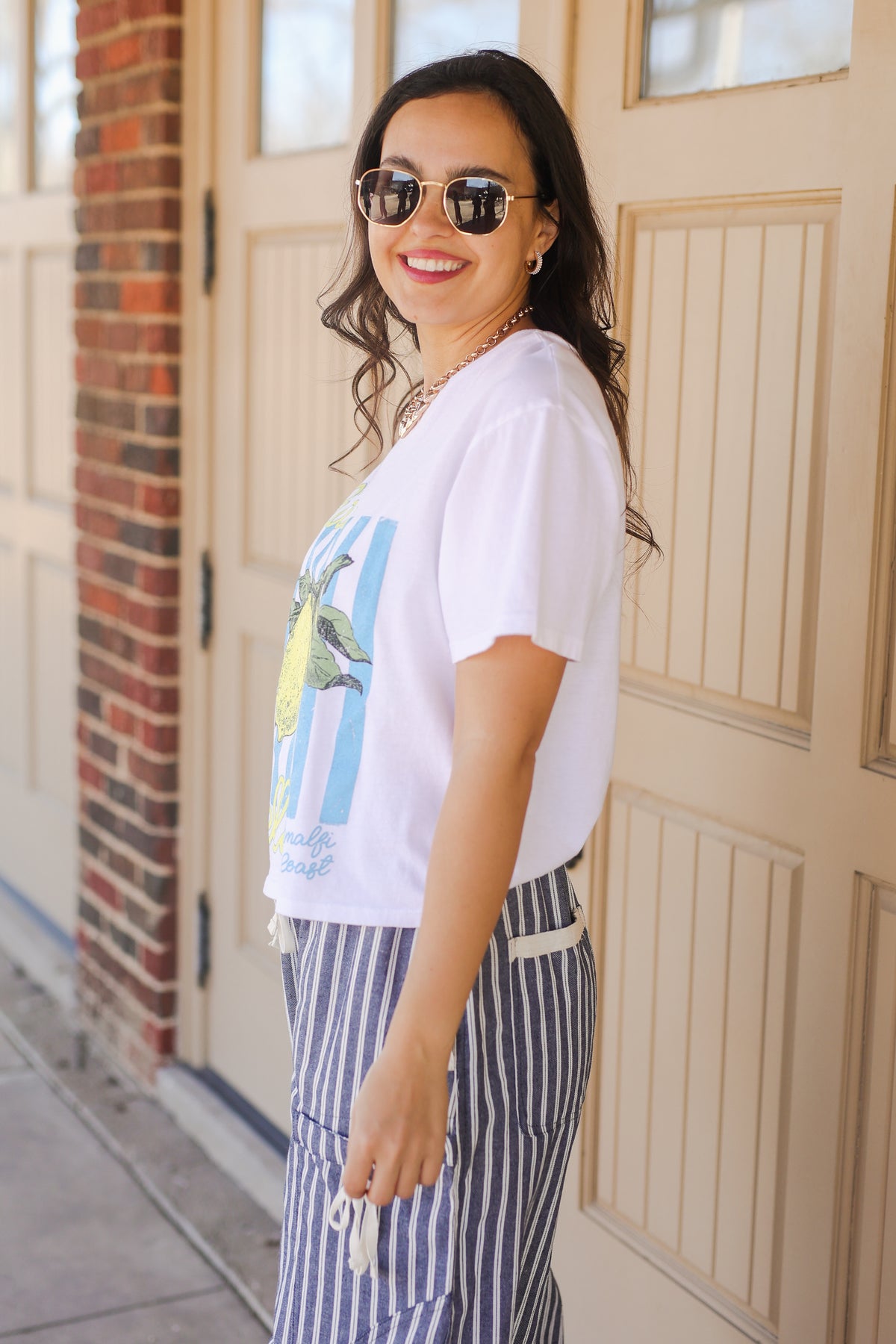 Woman wearing a white graphic t-shirt and striped pants standing in front of a door.