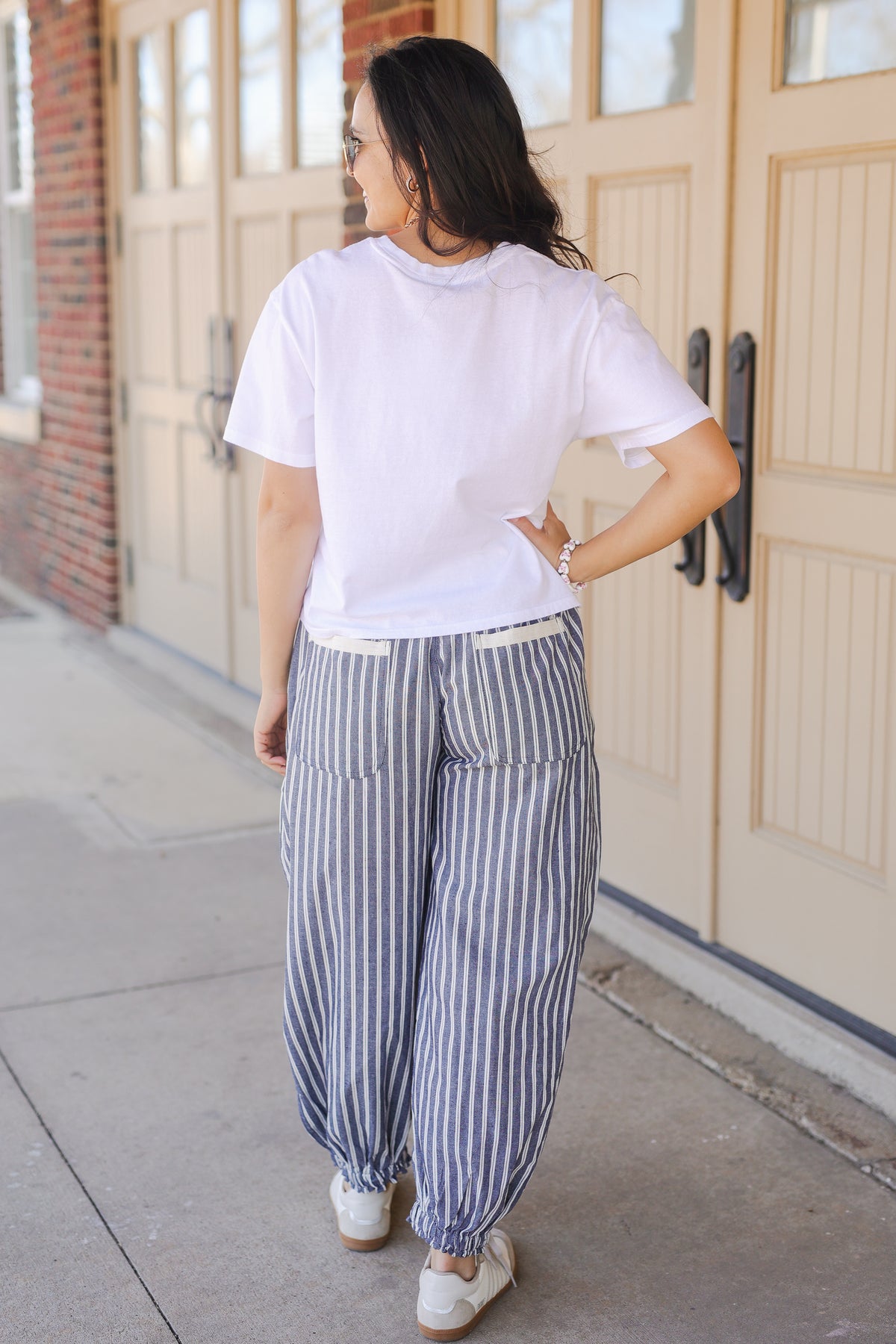 Person wearing a white t-shirt and blue striped pants standing on a sidewalk.
