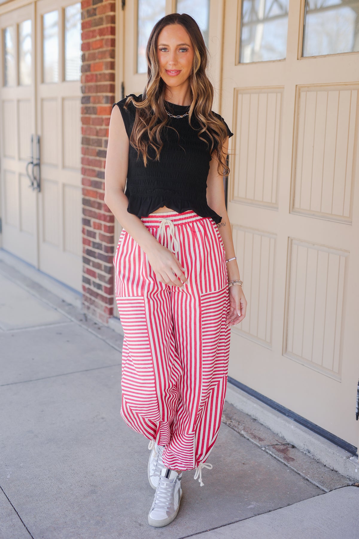 Woman wearing a black sleeveless top and red striped pants standing on a sidewalk.