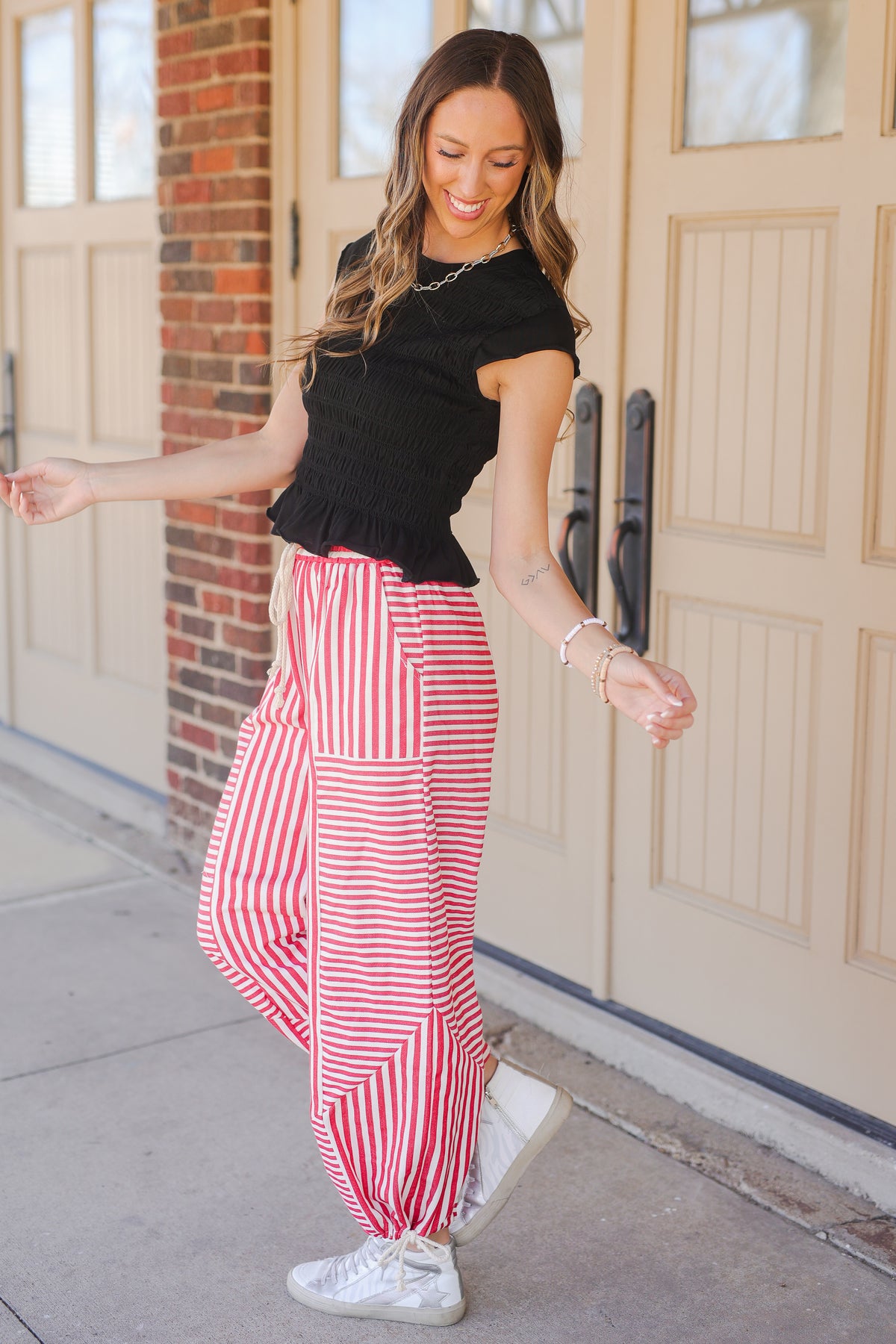 Woman wearing a black top and red striped pants standing in front of a door.