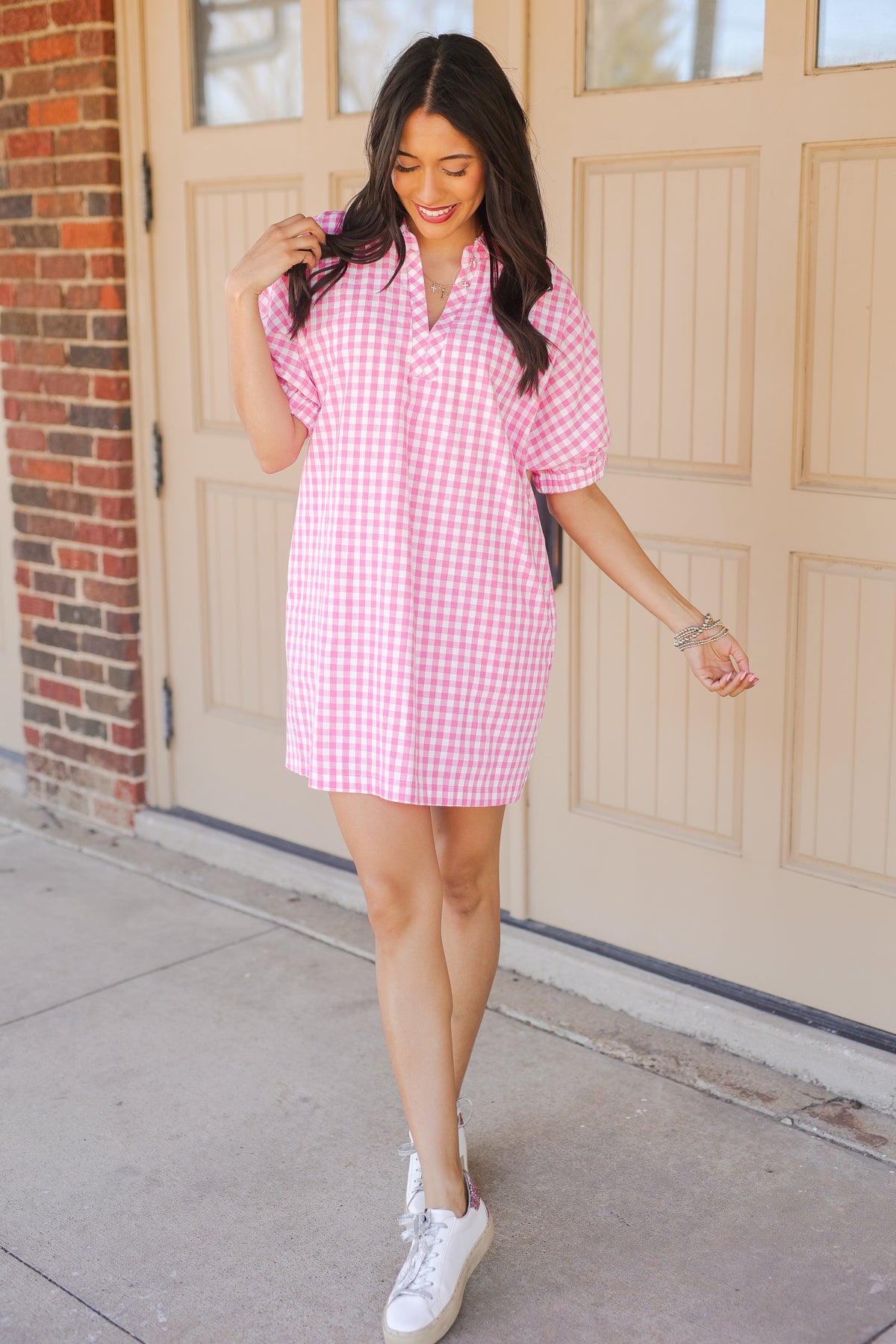 Woman wearing a pink checkered dress standing in front of a garage door.