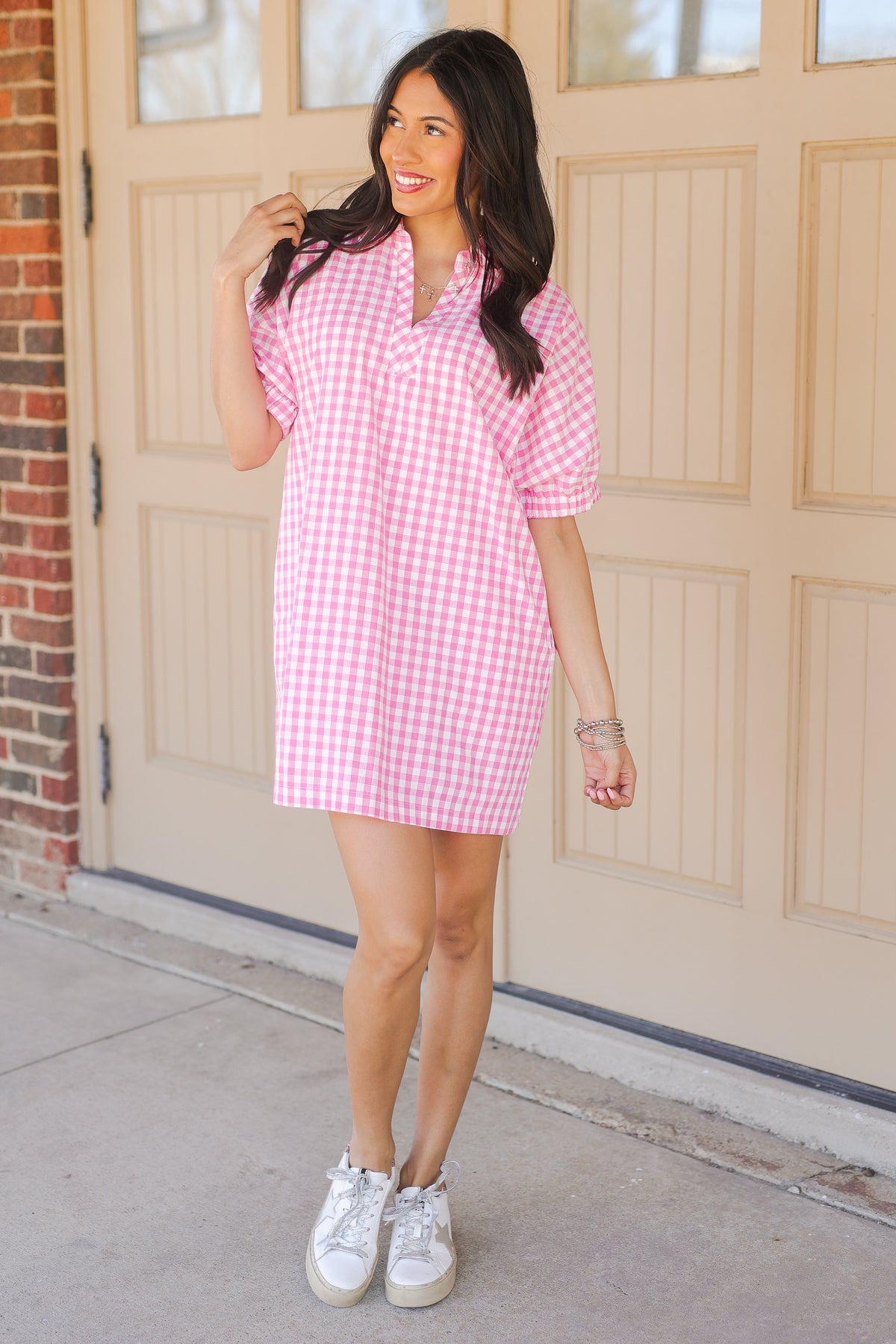 Woman wearing a pink checkered dress standing in front of a beige door.