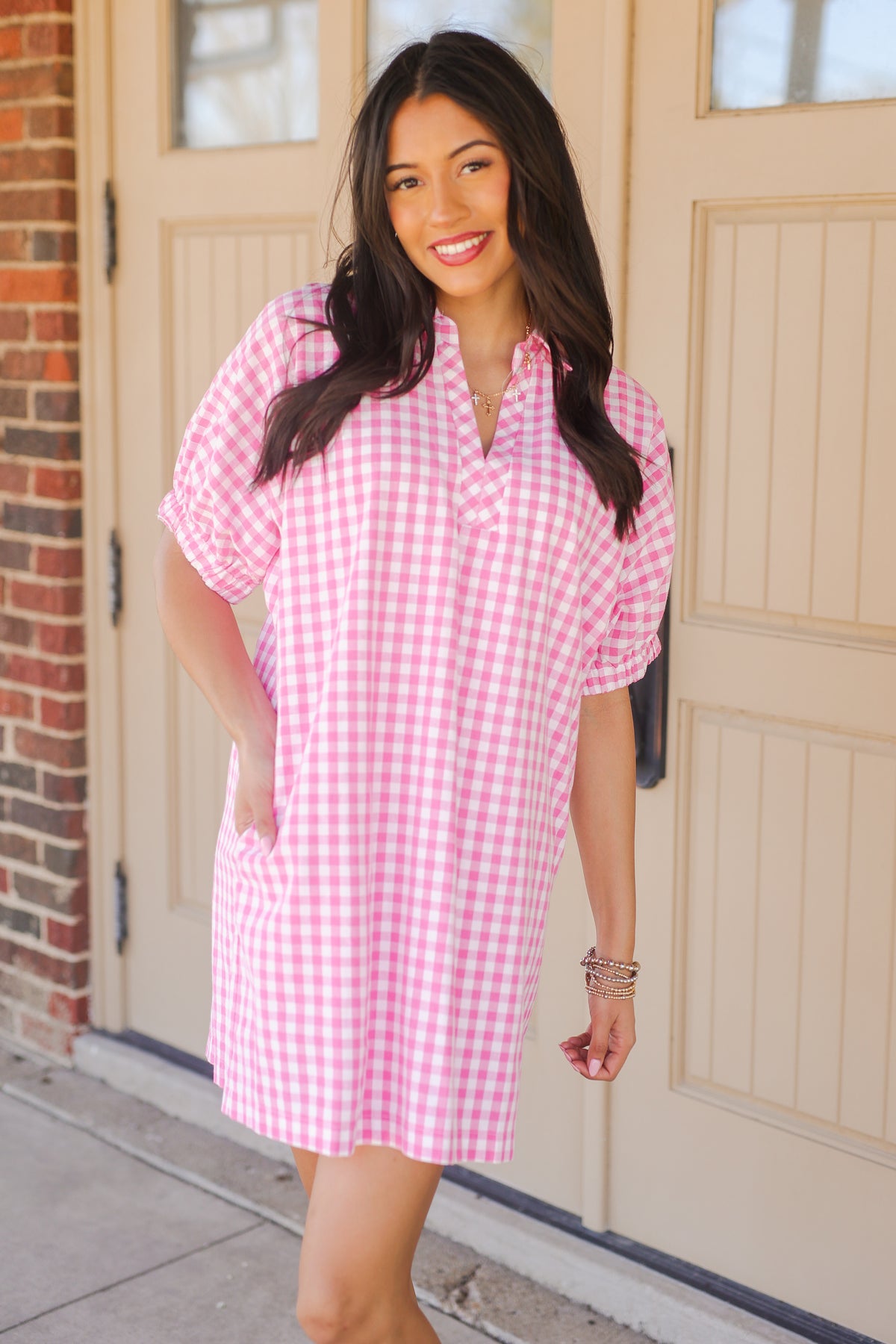 Woman wearing a pink checkered dress standing in front of a door.