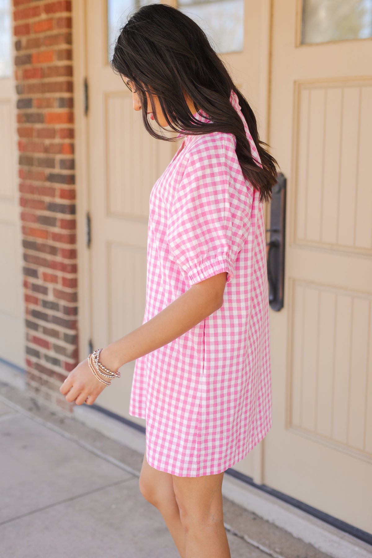 Woman wearing a pink checkered dress standing in front of a door.