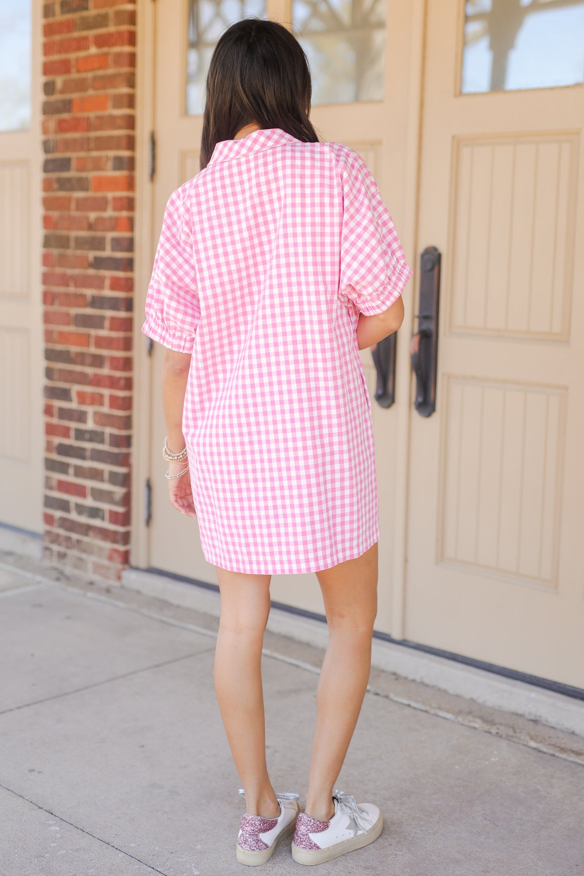 Person wearing a pink and white checkered dress standing in front of a door.