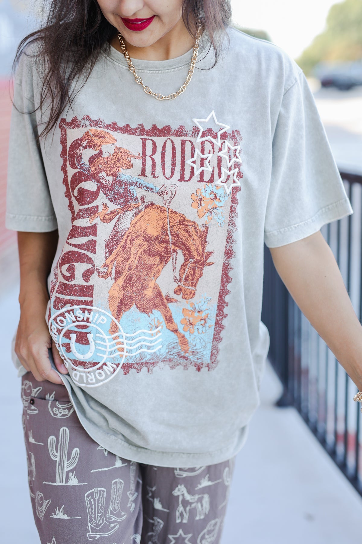 Person wearing a gray t-shirt with a rodeo graphic design outdoors.