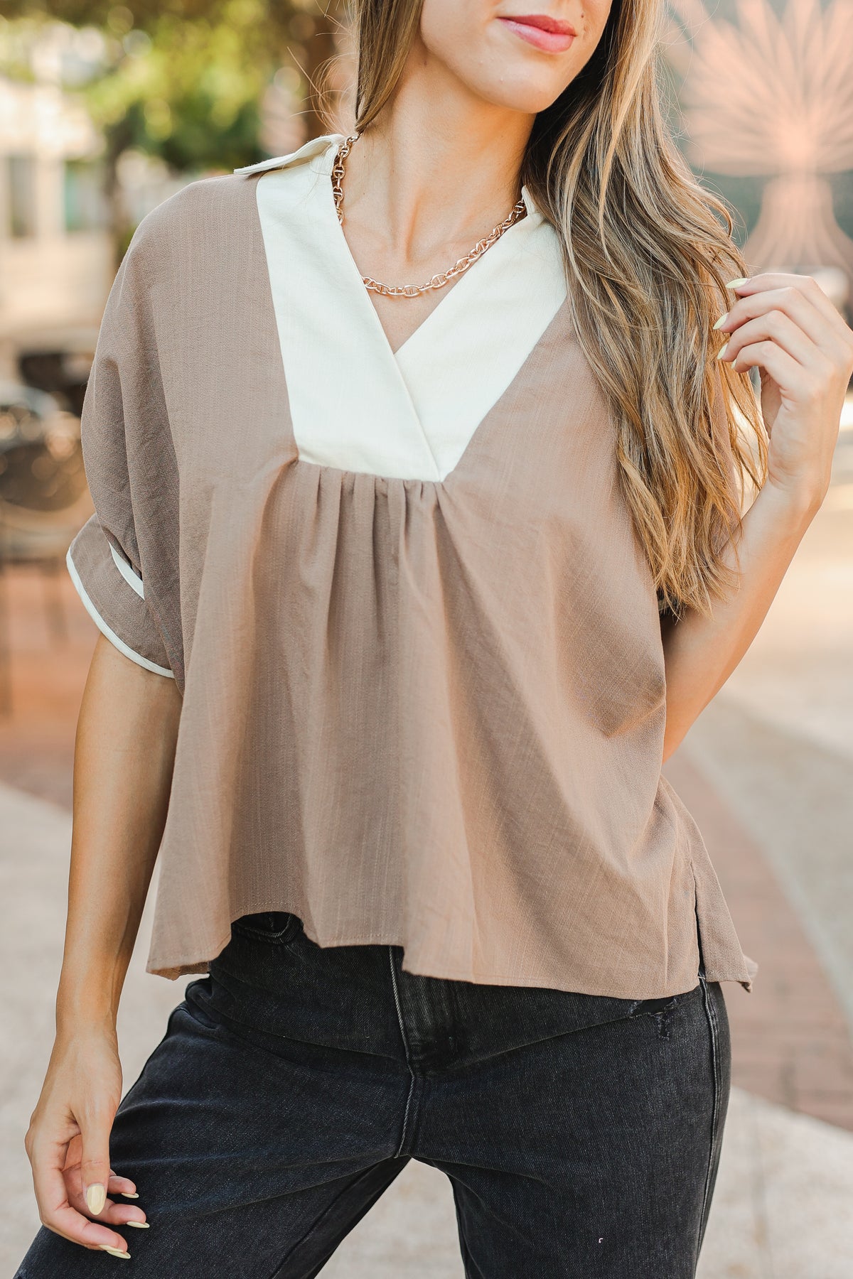 Woman wearing a beige blouse with white trim and black pants outdoors.