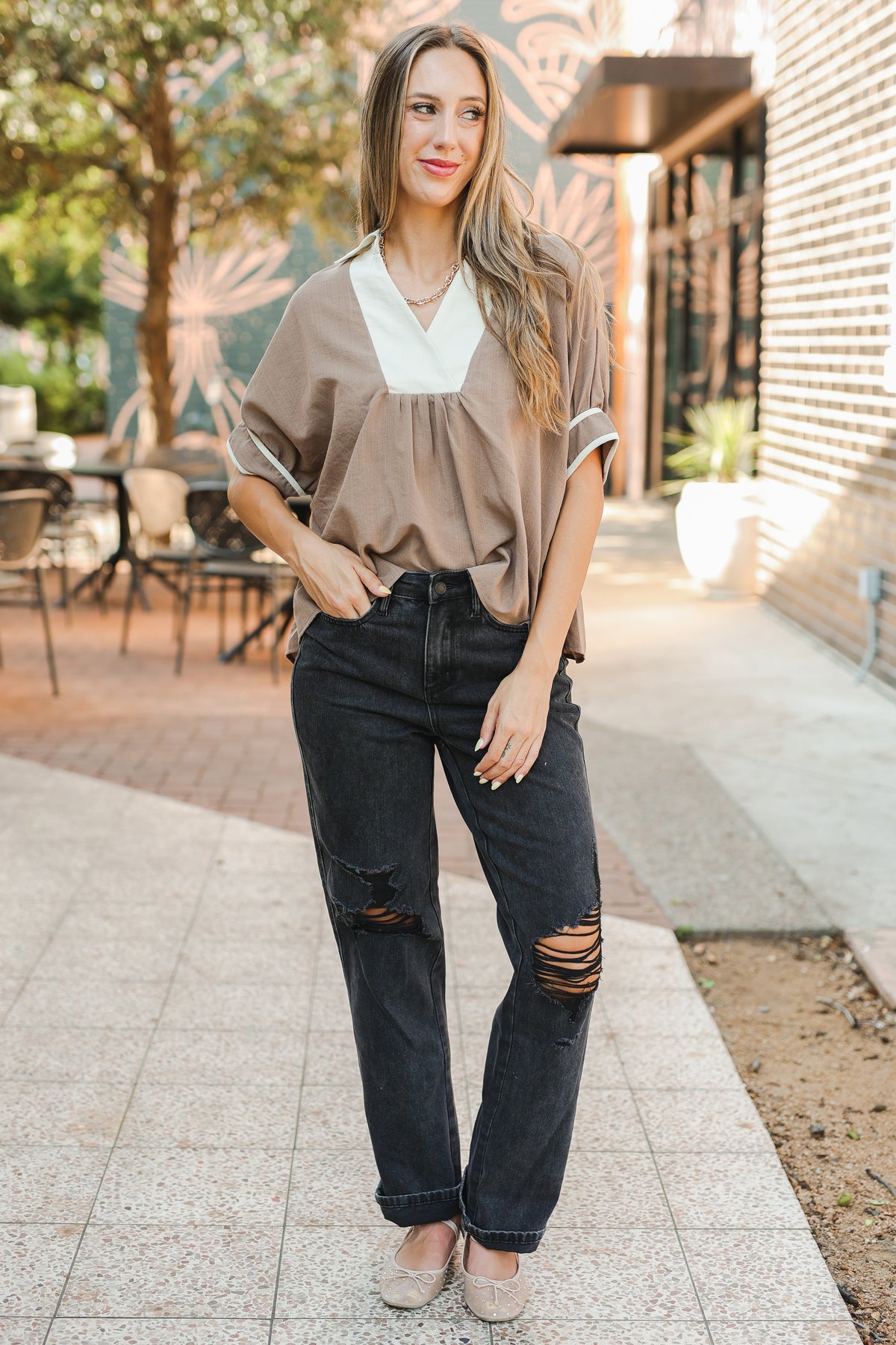 Woman wearing a beige blouse and black jeans standing outdoors.