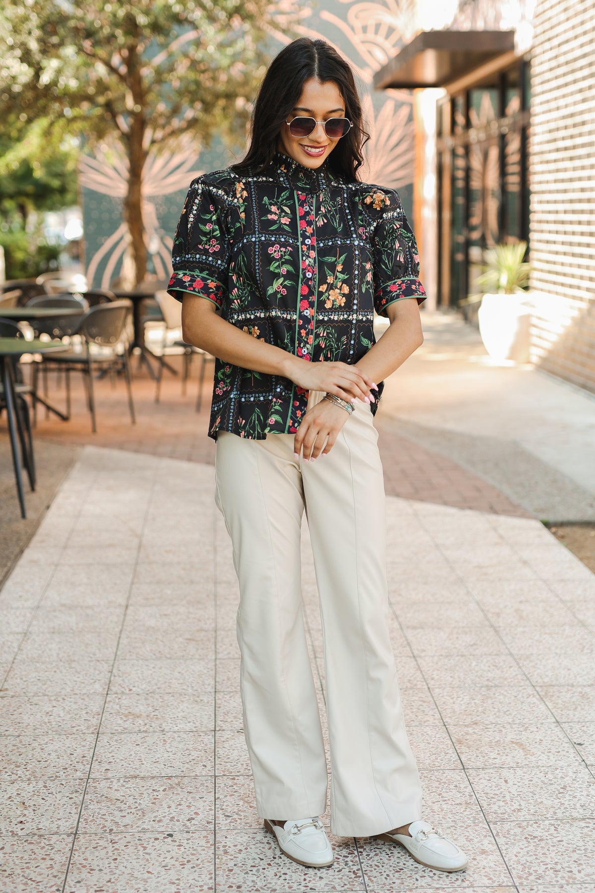 Woman wearing a patterned top and white pants outdoors.