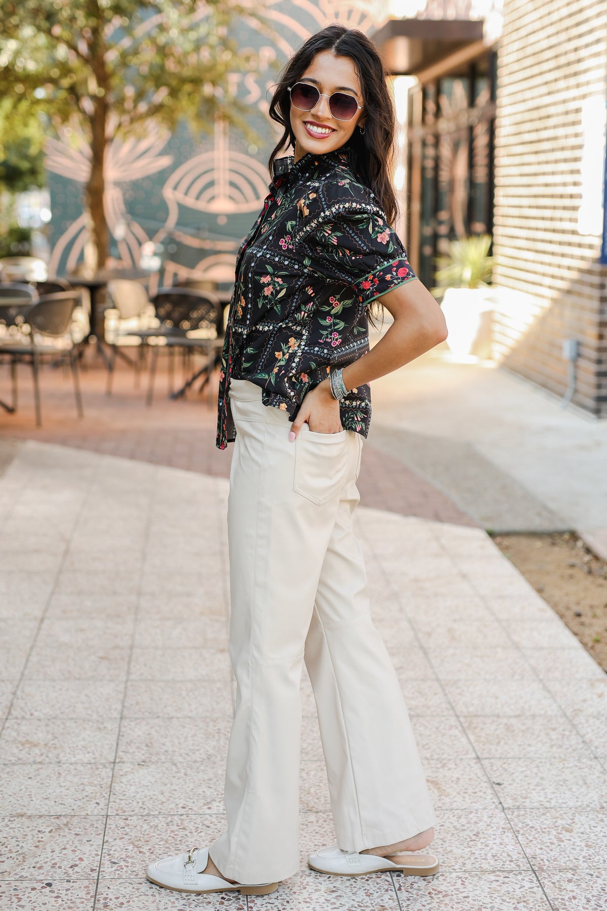 Woman wearing a floral blouse and white pants standing outdoors.