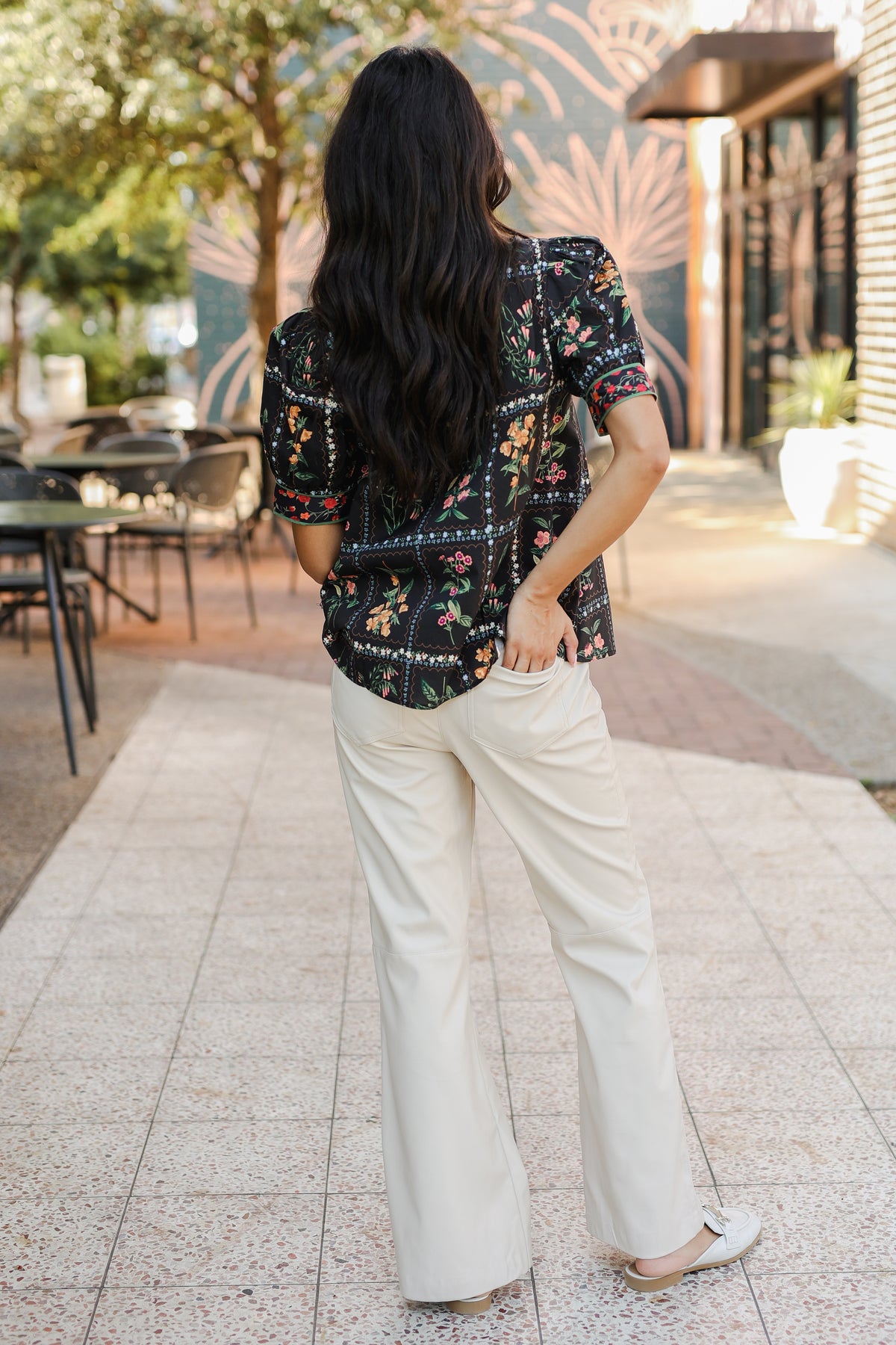 Woman wearing a floral blouse and white pants walking outdoors.
