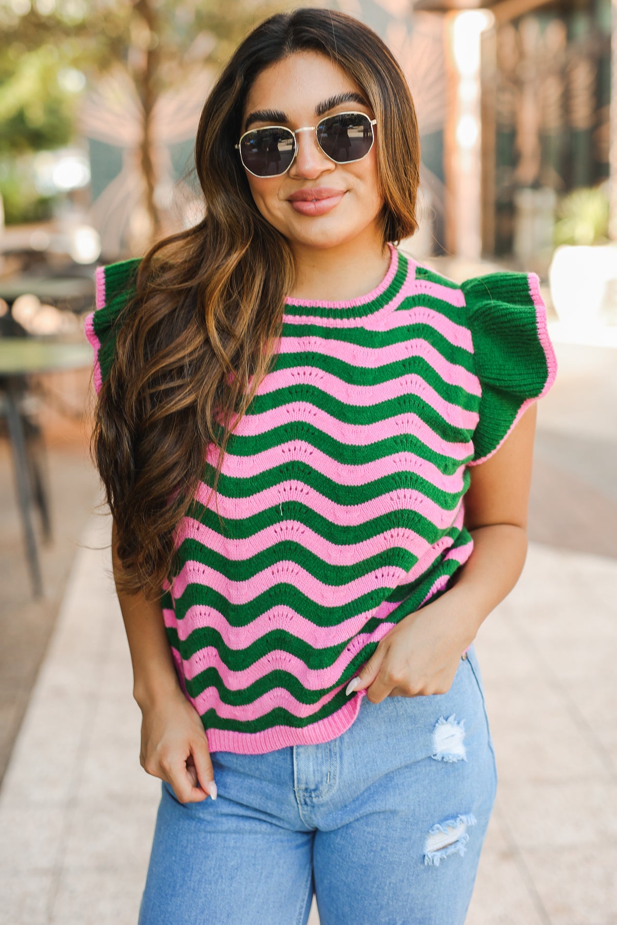 Woman wearing a green and pink striped sweater with ruffled sleeves outdoors.