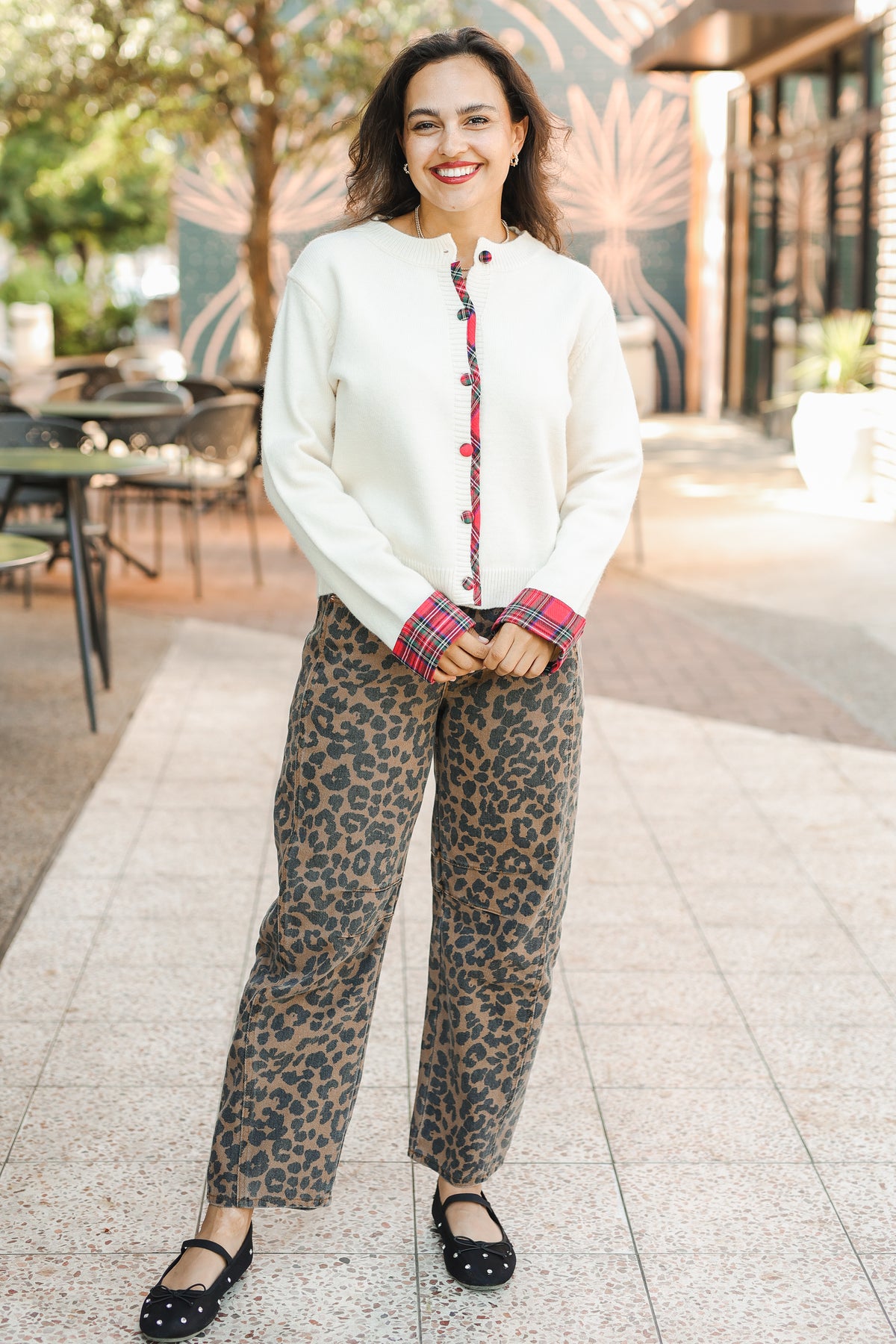 Woman wearing a white blouse with red buttons and leopard print pants outdoors.