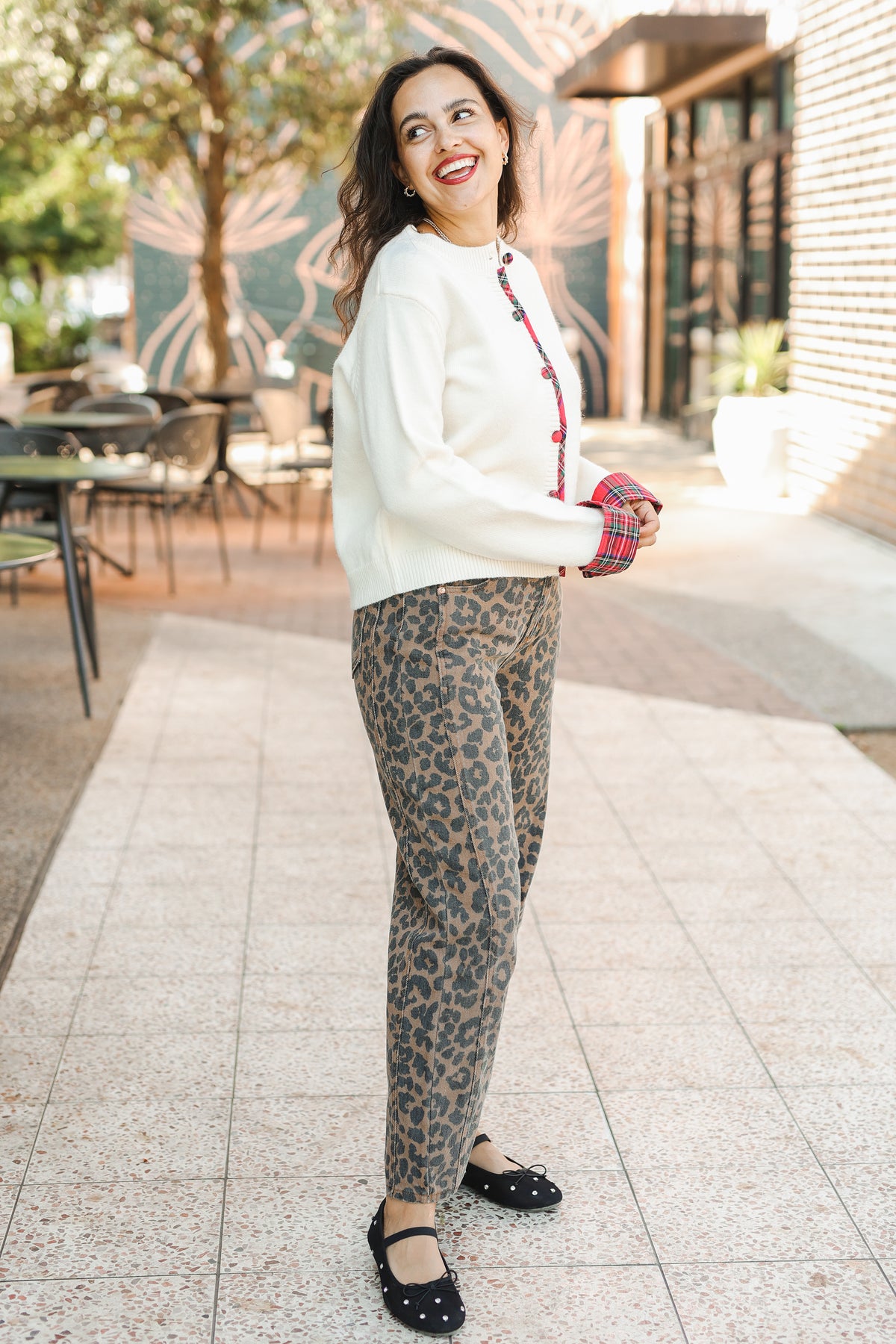 Woman in a white sweater and leopard print pants standing on a sidewalk.