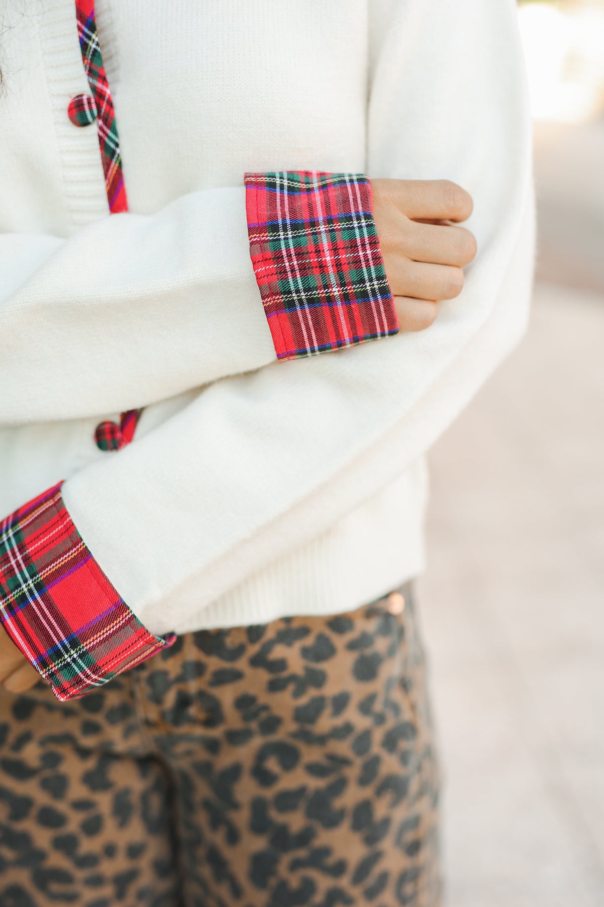 Close-up of a person wearing a white coat with red plaid cuffs and hem, paired with leopard print pants.