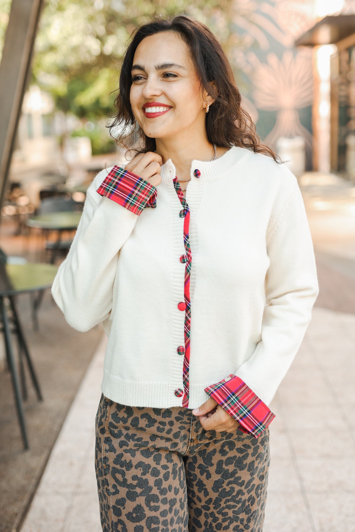 Woman wearing a white cardigan with red plaid accents and leopard print pants outdoors.