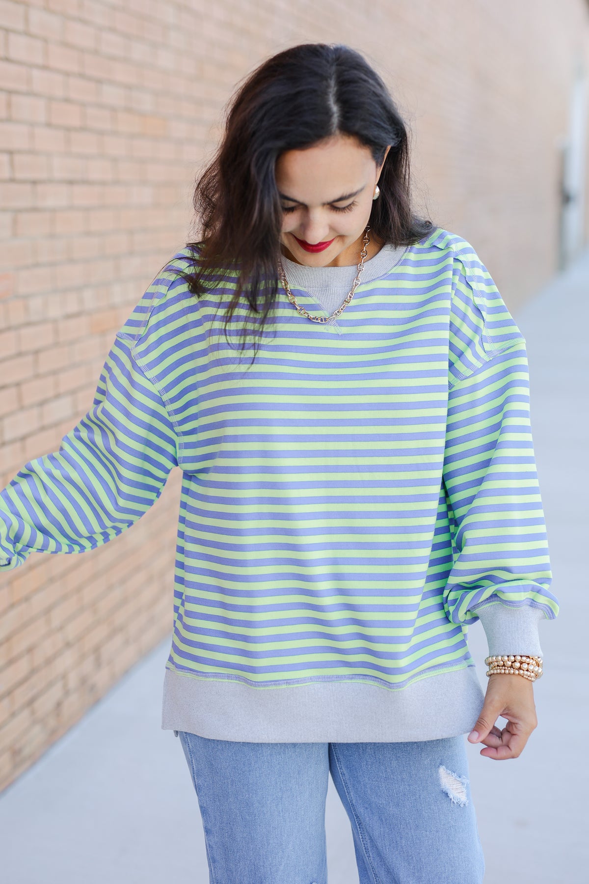 Woman wearing a striped sweater and jeans against a brick wall.