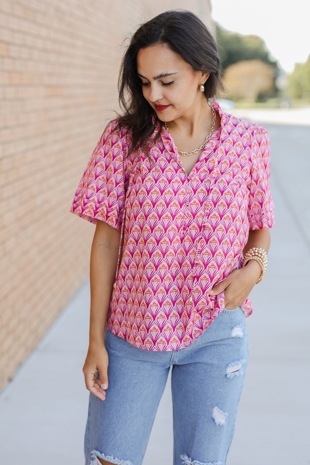 Woman wearing a pink patterned blouse and blue jeans outdoors.