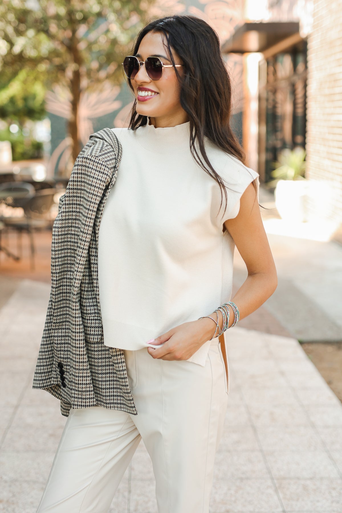 Woman wearing a white sleeveless top and plaid blazer outdoors.