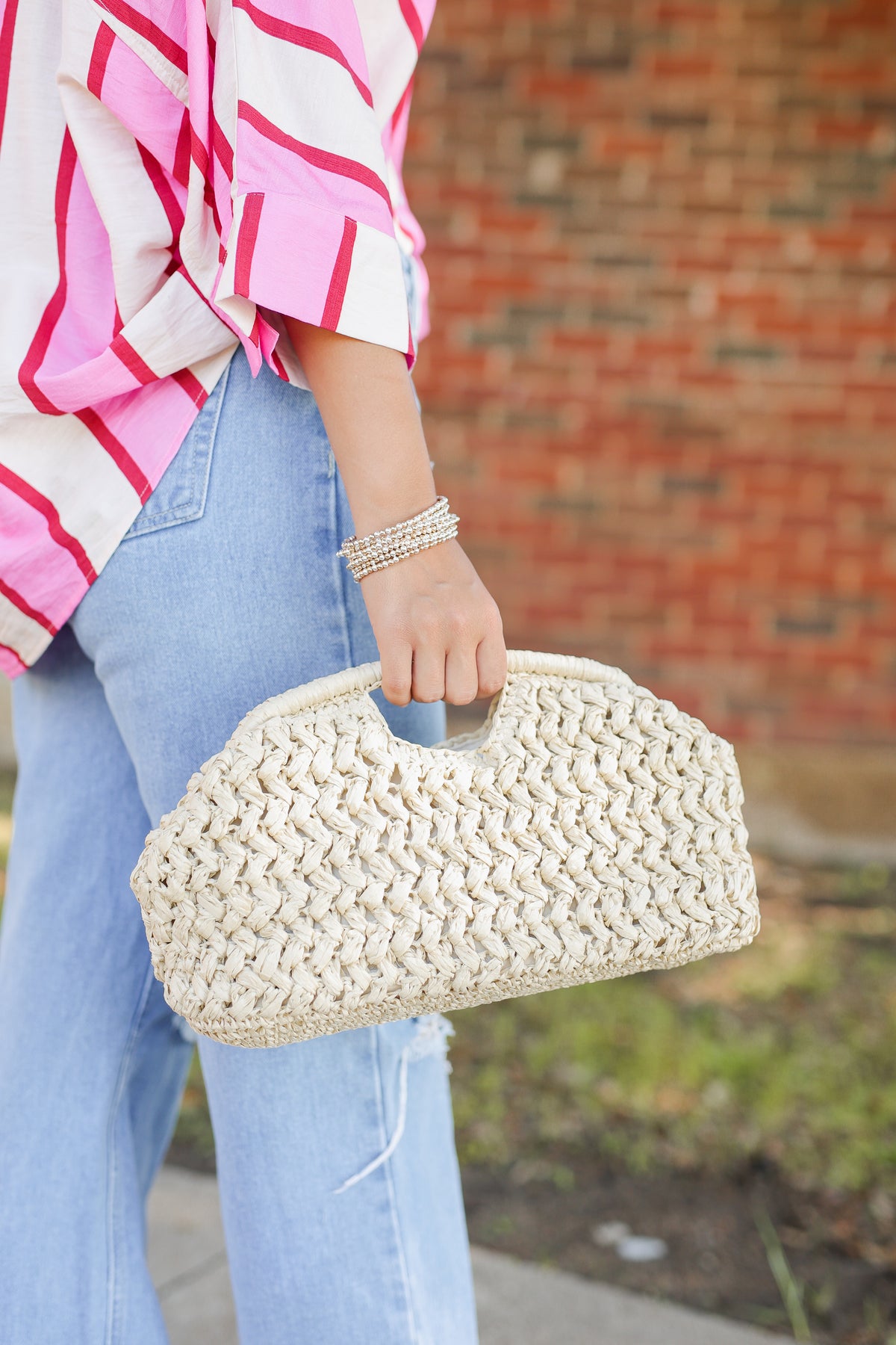 Person holding a woven beige clutch with a blurred background