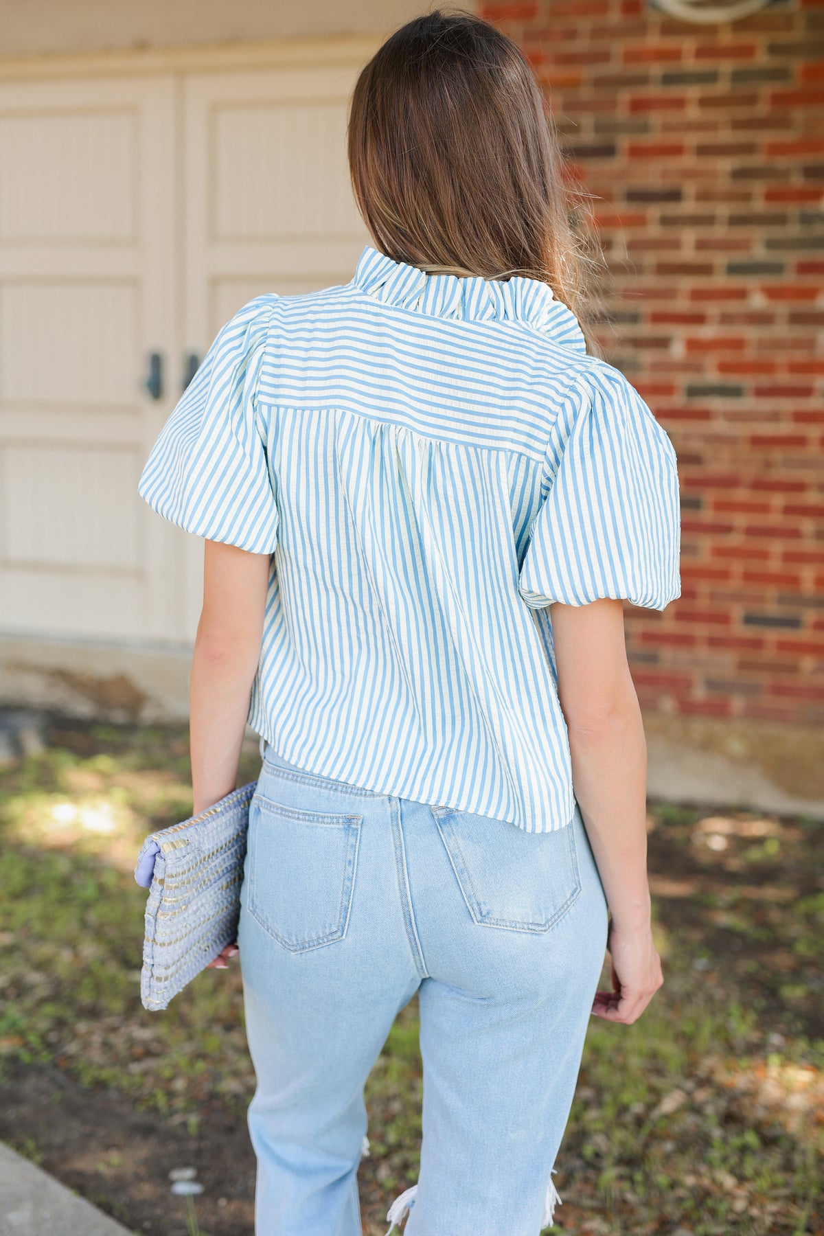 Woman wearing a blue and white striped shirt and light blue jeans, standing in front of a garage.