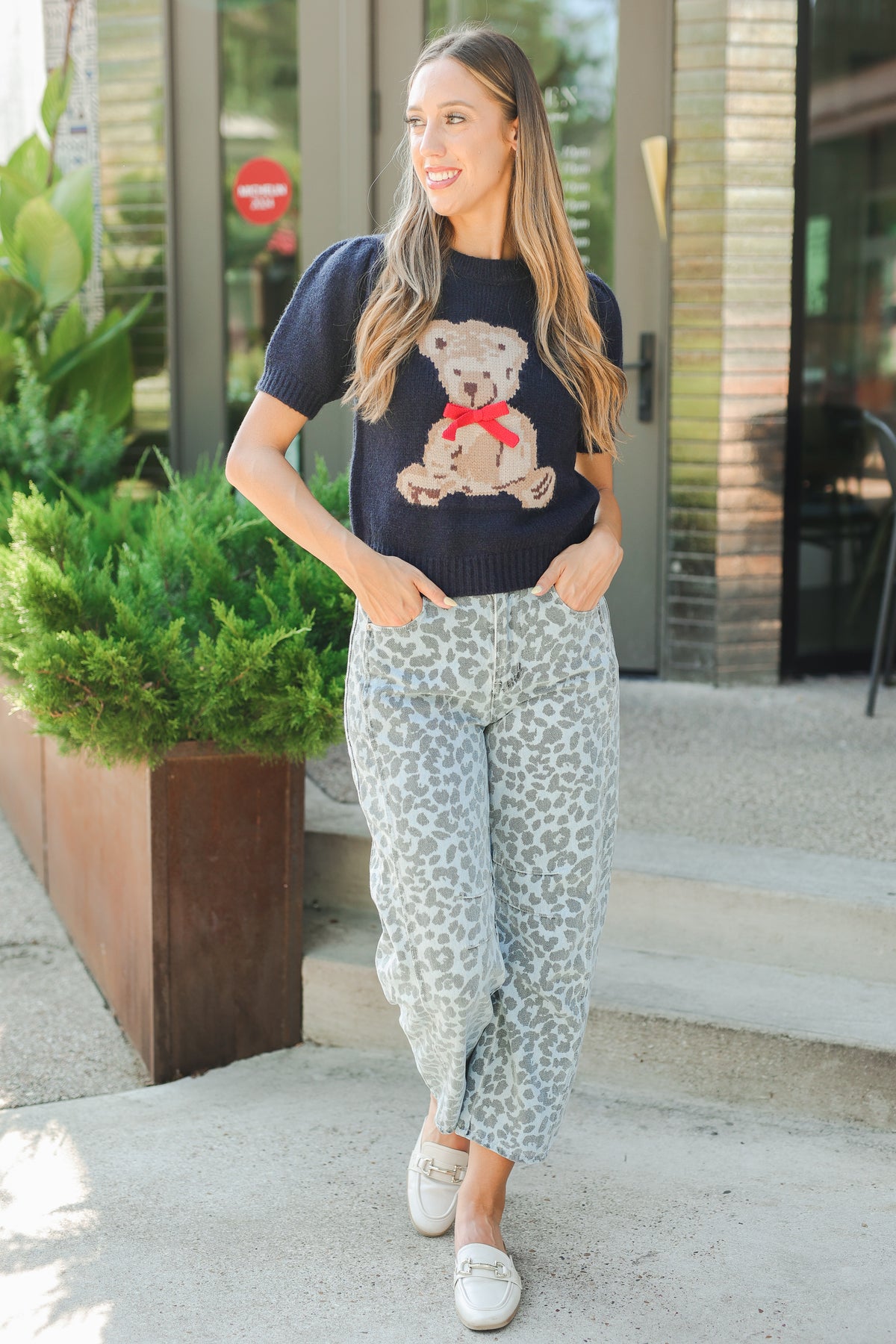 Woman wearing a navy t-shirt with a teddy bear graphic and light blue patterned pants, standing outdoors.
