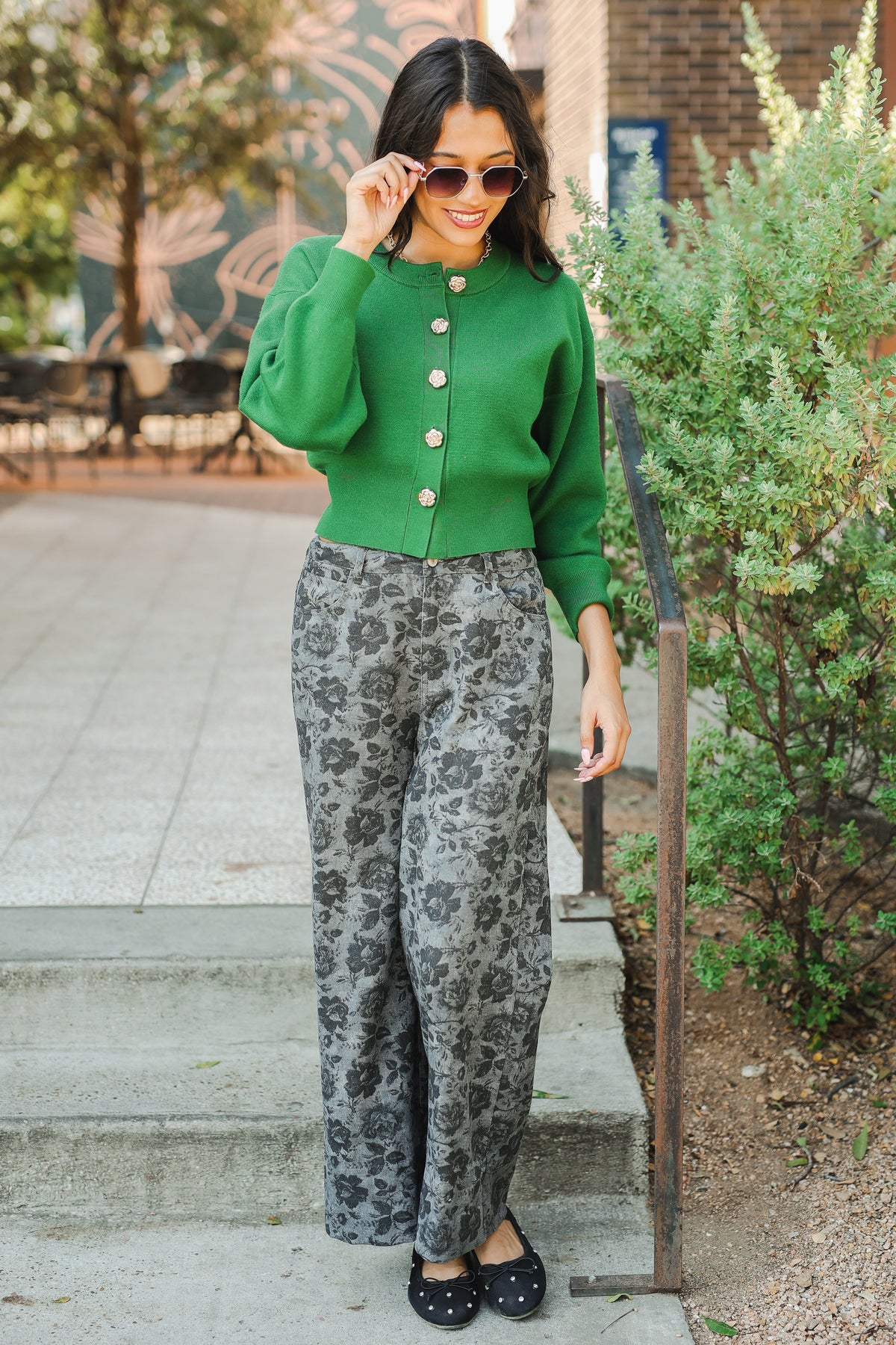Woman wearing a green cardigan and patterned pants standing outdoors.