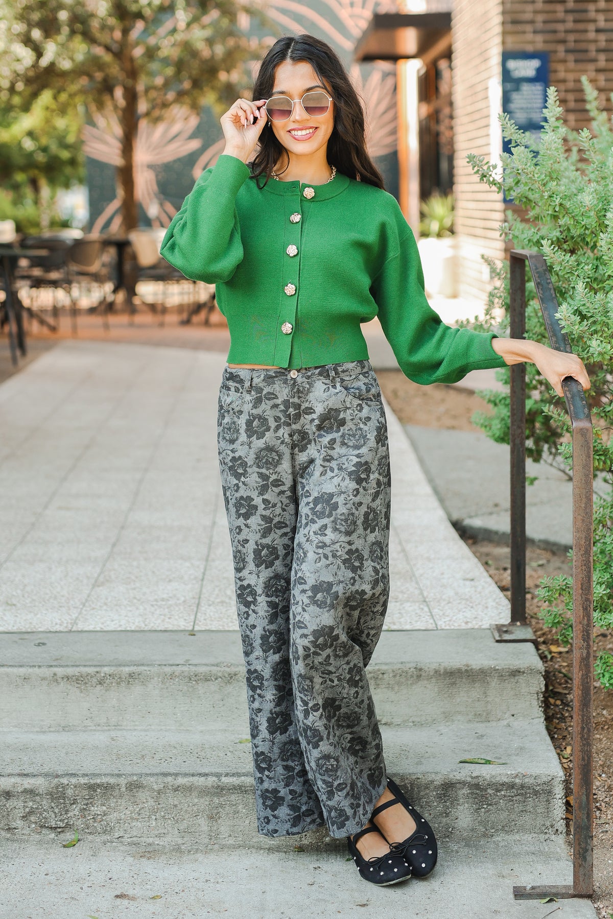 Woman in a green cardigan and patterned pants standing outdoors.