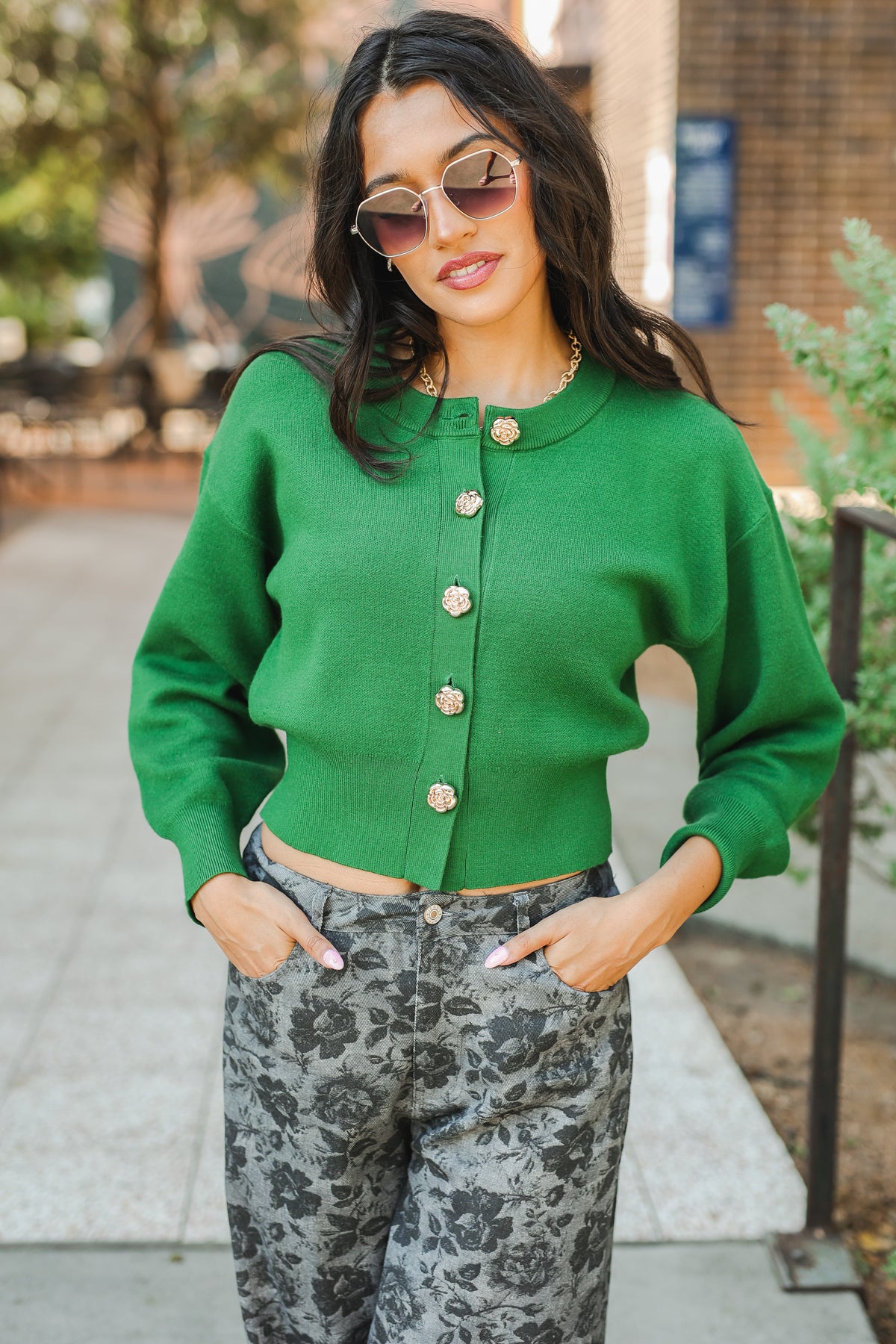 Woman wearing a green cardigan and patterned pants outdoors.
