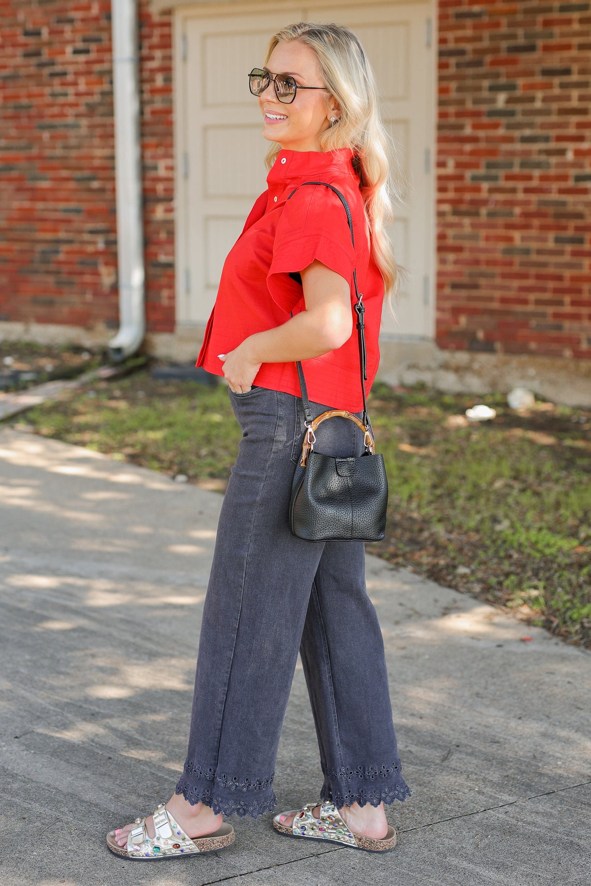 Blonde model wearing a red top with black denim pants carrying a black purse.