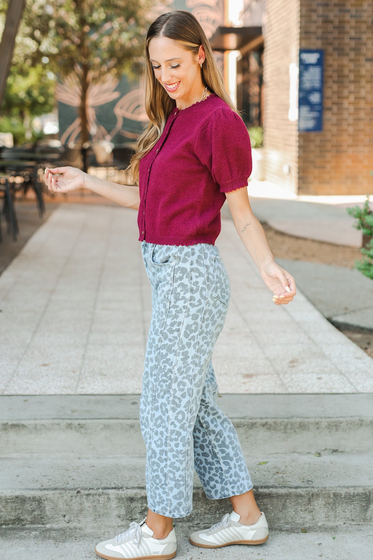 Woman in a red top and light blue patterned pants standing on steps outdoors.
