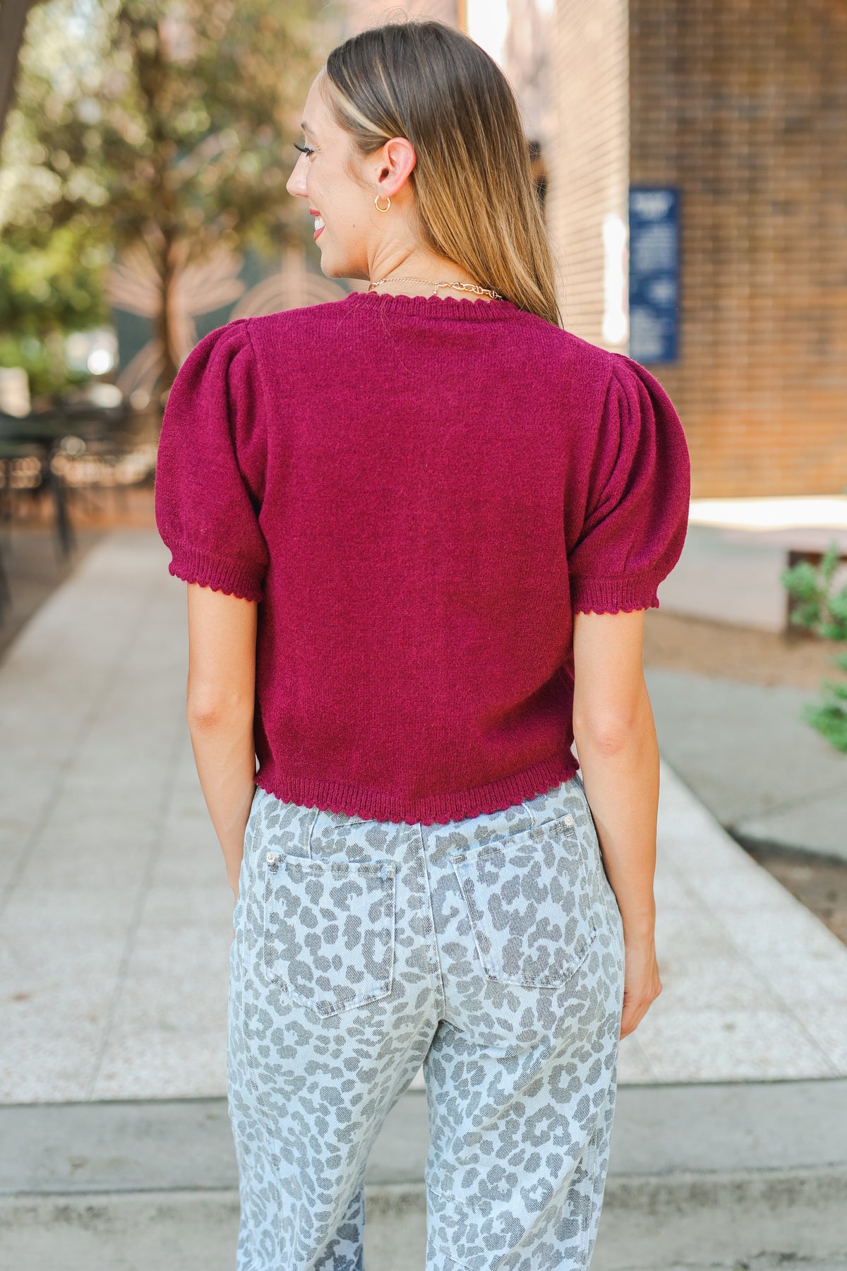 Woman wearing a magenta sweater and patterned pants walking outdoors.