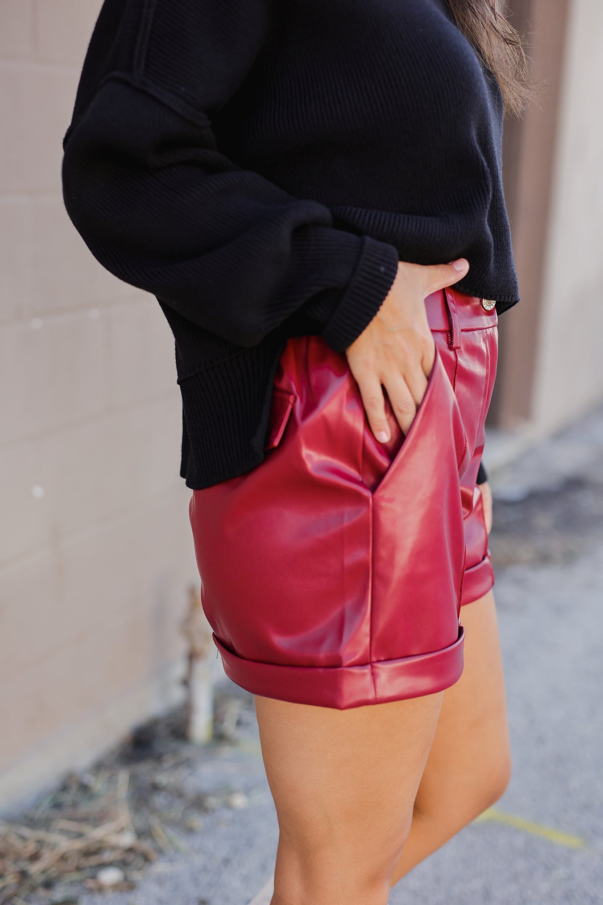 Person wearing a black sweater and red leather shorts against a neutral background