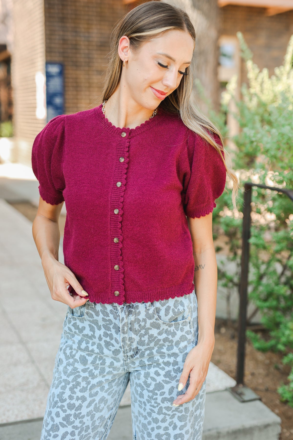 Woman wearing a magenta cardigan with short sleeves and light blue patterned pants outdoors.