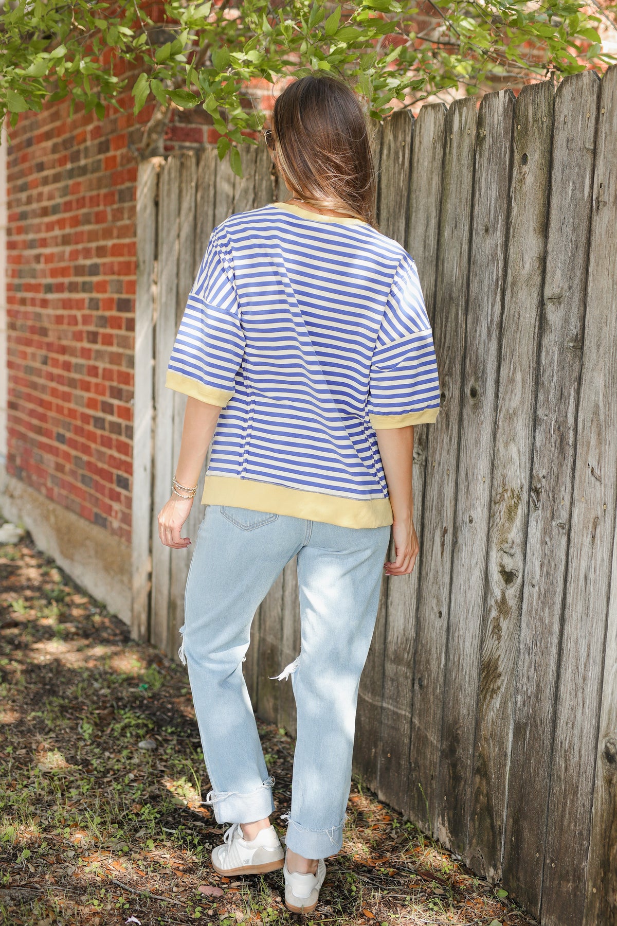 Person wearing a blue and white striped shirt and light blue jeans standing against a wooden fence.
